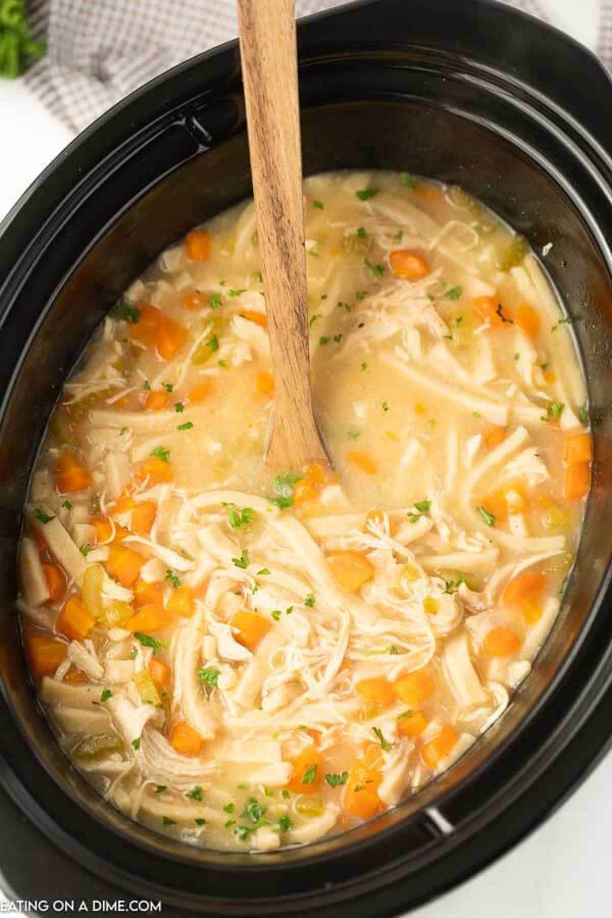 Close up image of chicken noodle soup with a brown serving spoon in the crockpot.