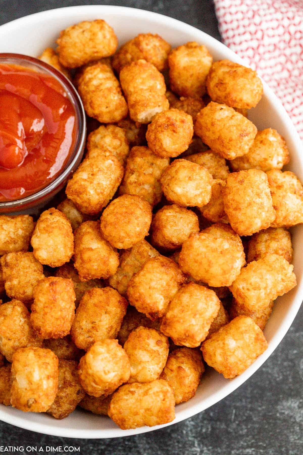 Crispy Tator Tots on a white platter with a bowl of ketchup on the side