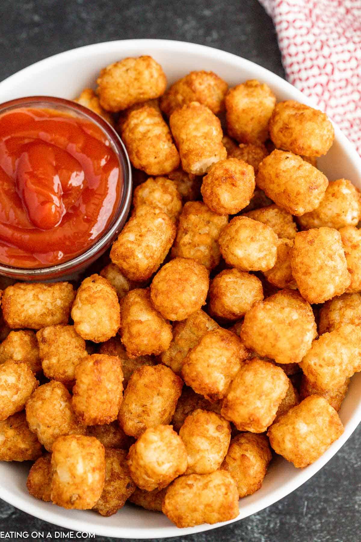 Crispy tator tots on a white platter with a bowl of ketchup on the side