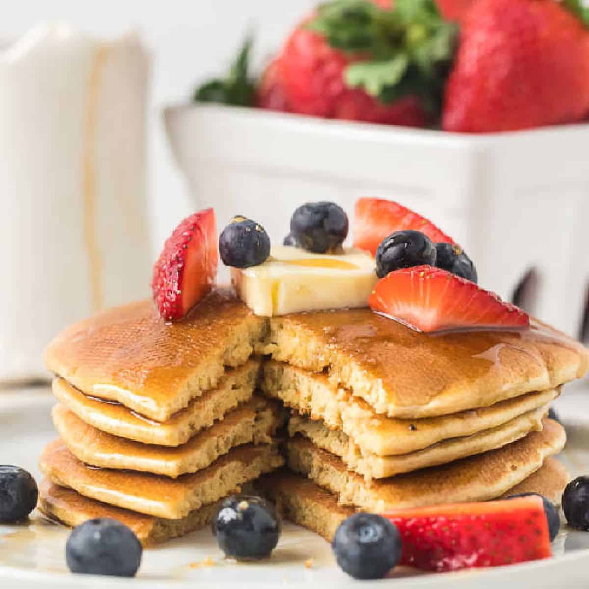 Gluten free pancakes stacked on a plate topped with butter, strawberries and blueberries