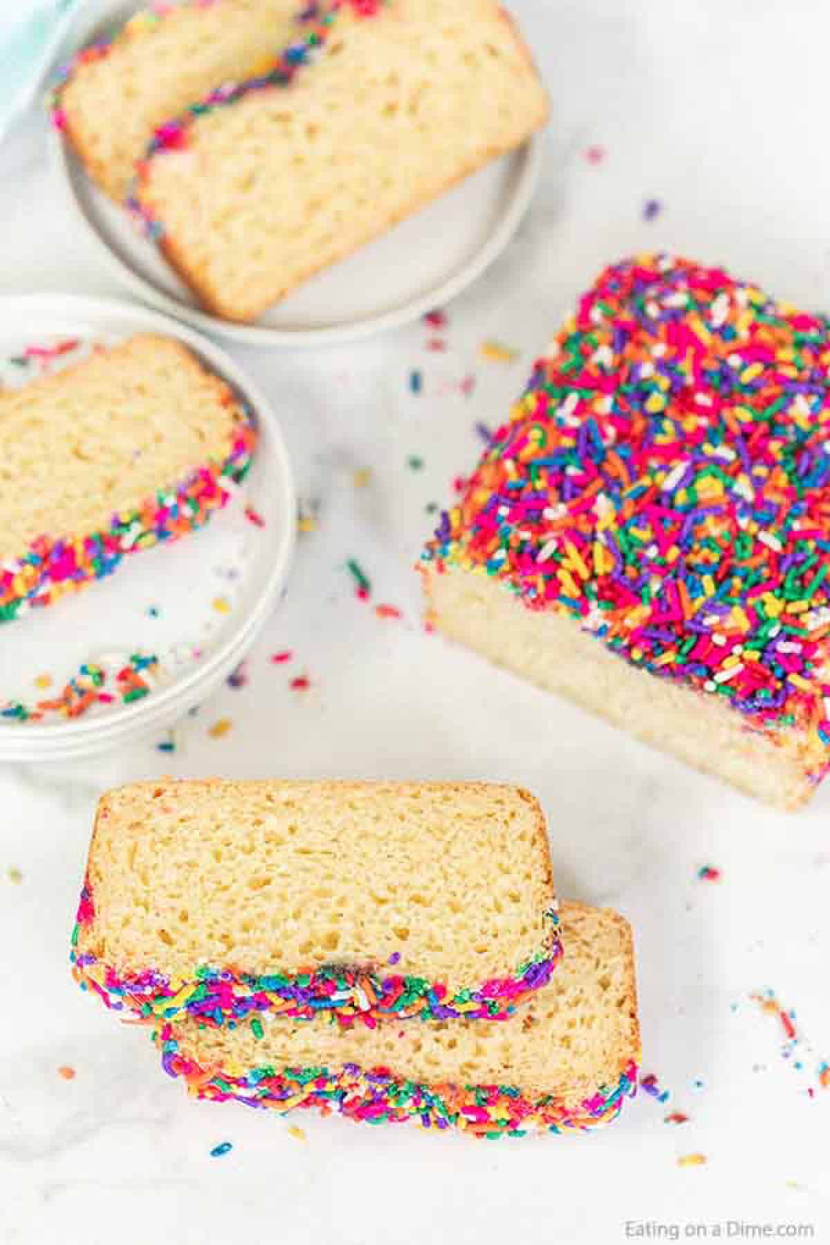 Slice of ice cream bread topped with sprinkles on white plates with a side of loaf of bread