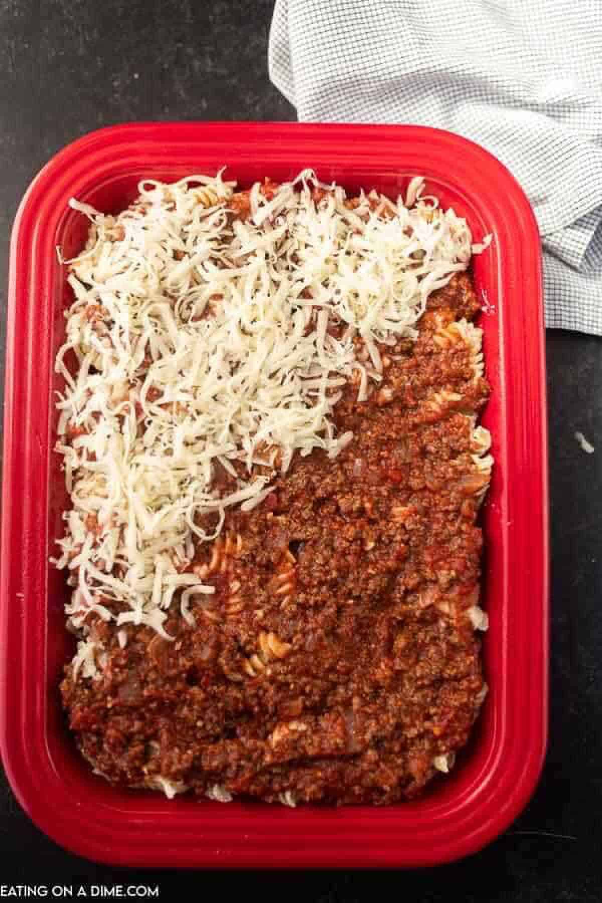 Shredded cheese top the meat sauce in the red casserole dish