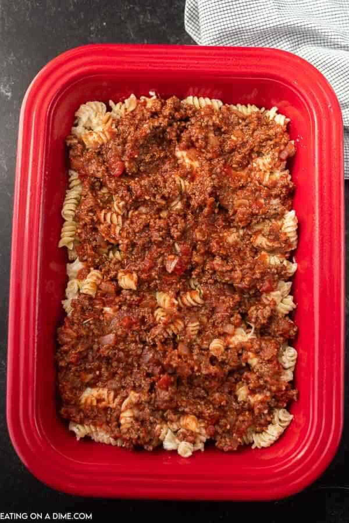 Meat sauce topped with pasta in the red casserole dish