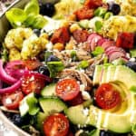 A vibrant salad bowl filled with an assortment of colorful ingredients, including sliced avocado, cherry tomatoes, cucumber, pickled onions, blueberries, roasted cauliflower, radishes, and chunks of roasted sweet potato. Topped with crumbled feta cheese, it's perfect for those who love diverse Rice Bowl Recipes.