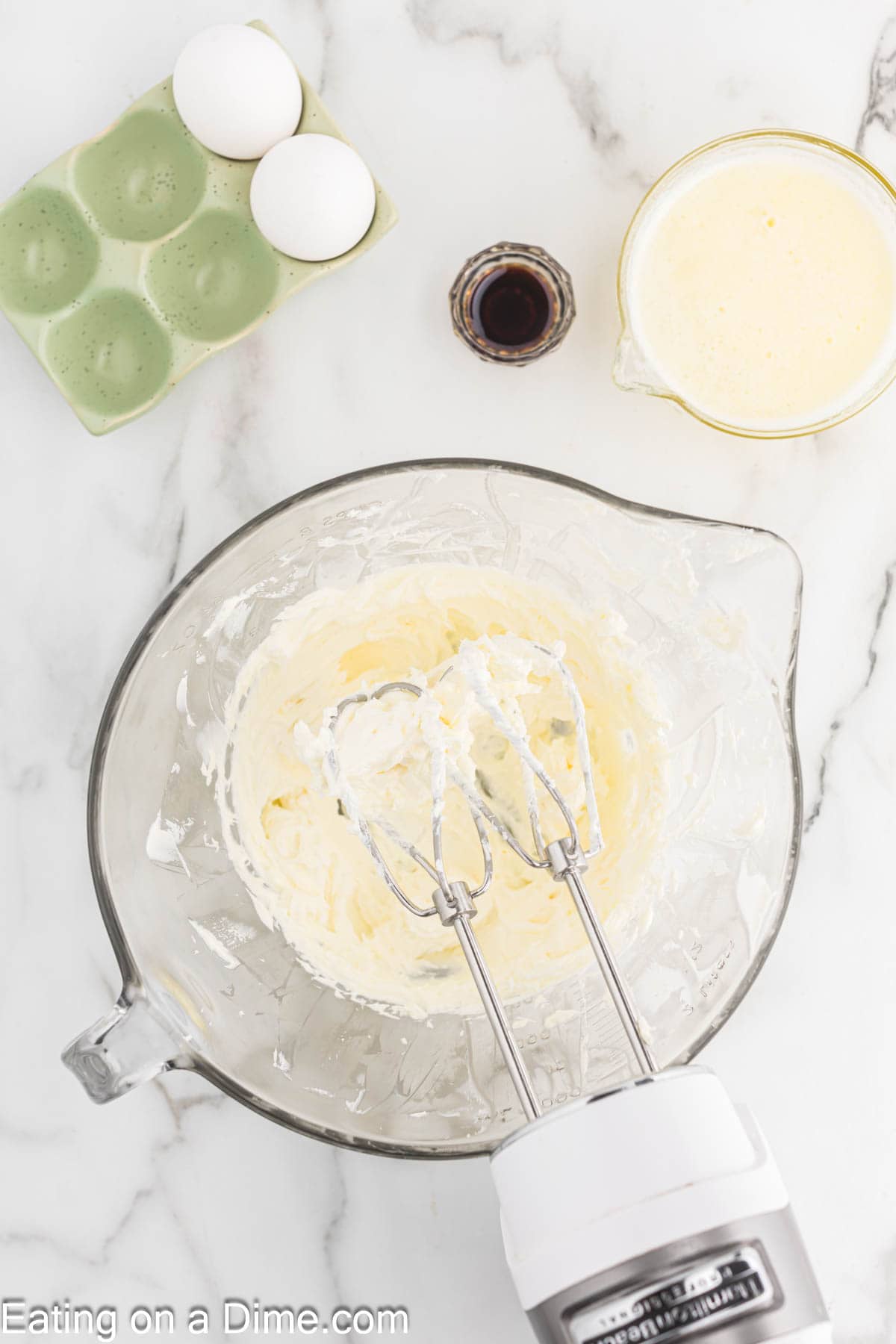 Beating the cream cheese in a bowl with a hand mixer with a side of egg, vanilla extract and melted butter