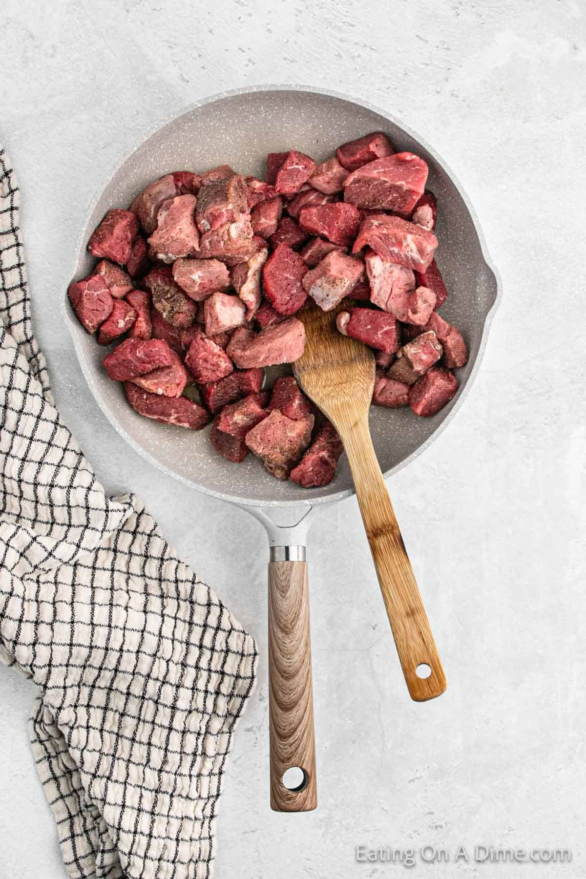 Diced seasoned steak in a skillet with a wooden spoon