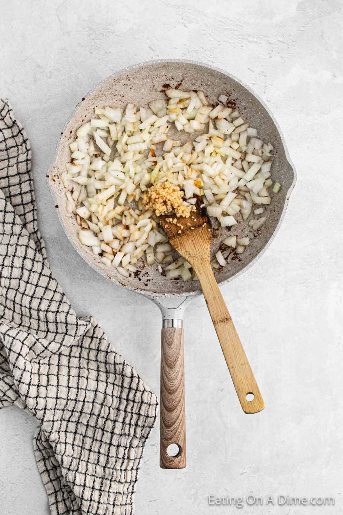 Diced onions with garlic in a skillet with a wooden spoon