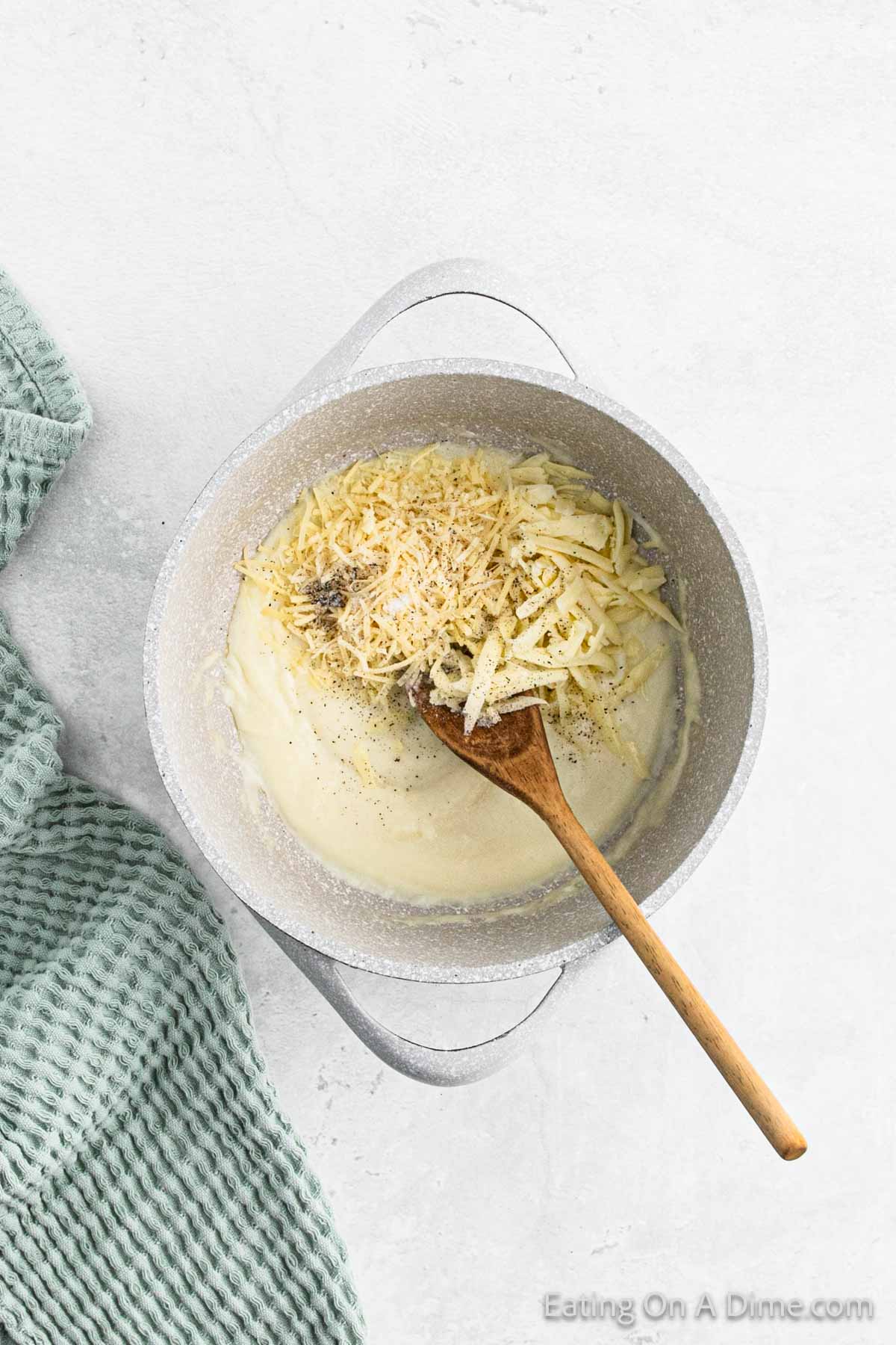 Mixing in broth with the grated cheese in the large pot with a wooden spoon