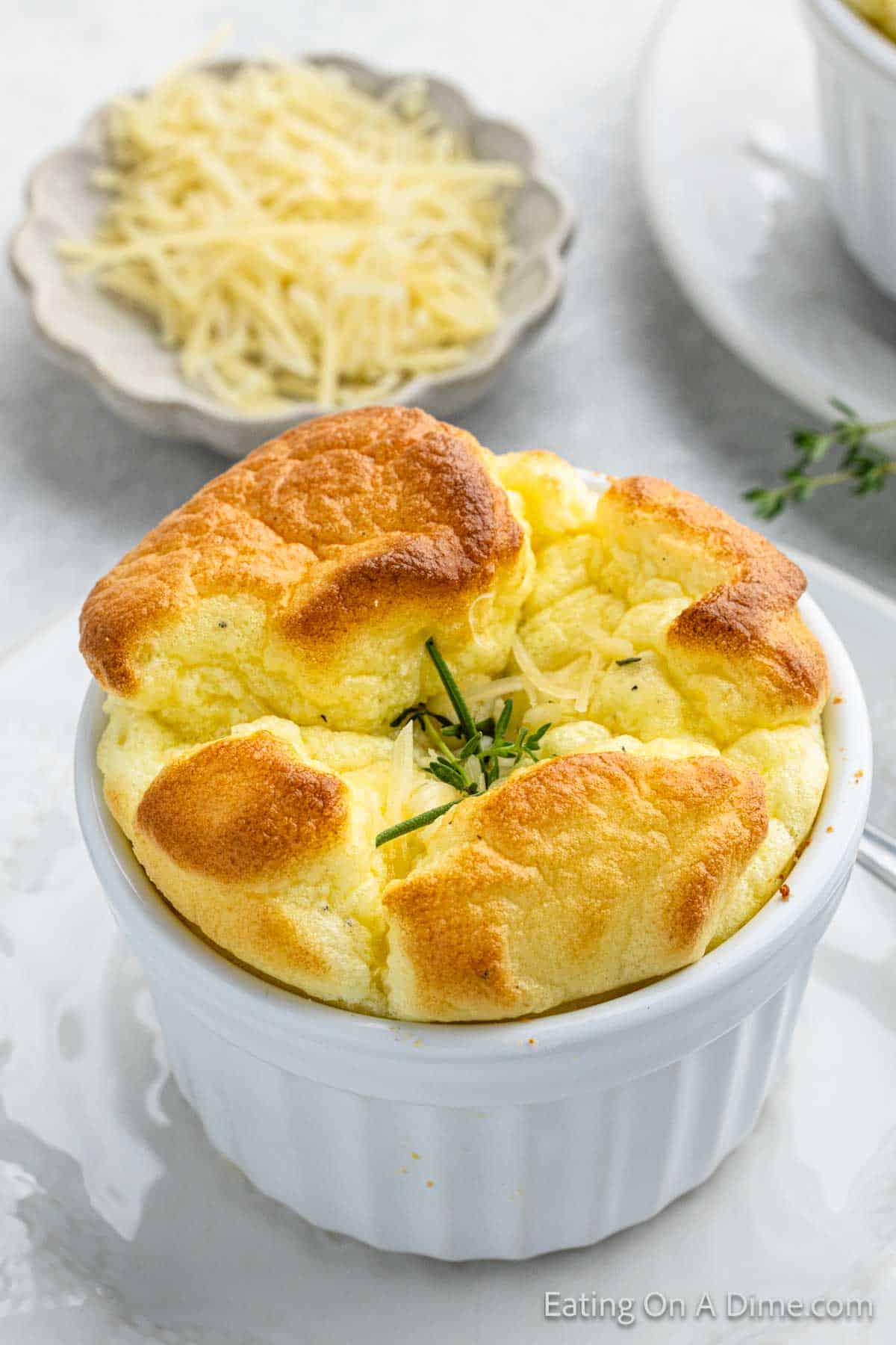 Baked egg souffle in a white ramekin with shredded cheese on a white plate