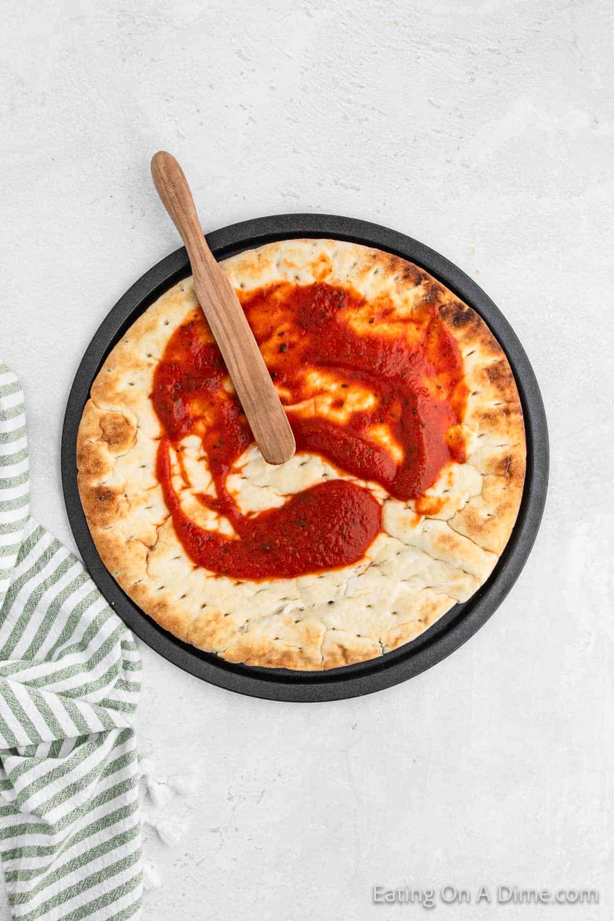 Spreading pizza sauce on pizza crust on a pan with wooden spoon