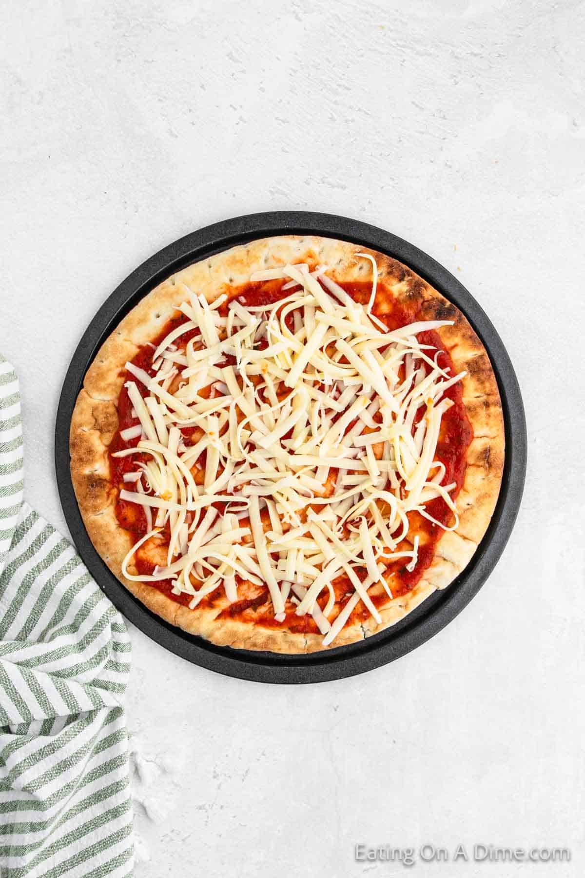 Pizza crust on pizza pan topped with pizza sauce and shredded cheese