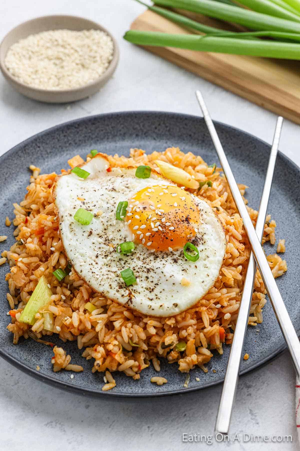 Kimchi Fried Rice Topped with a fried egg, sesame seeds and chopped green onions with chopsticks on the side