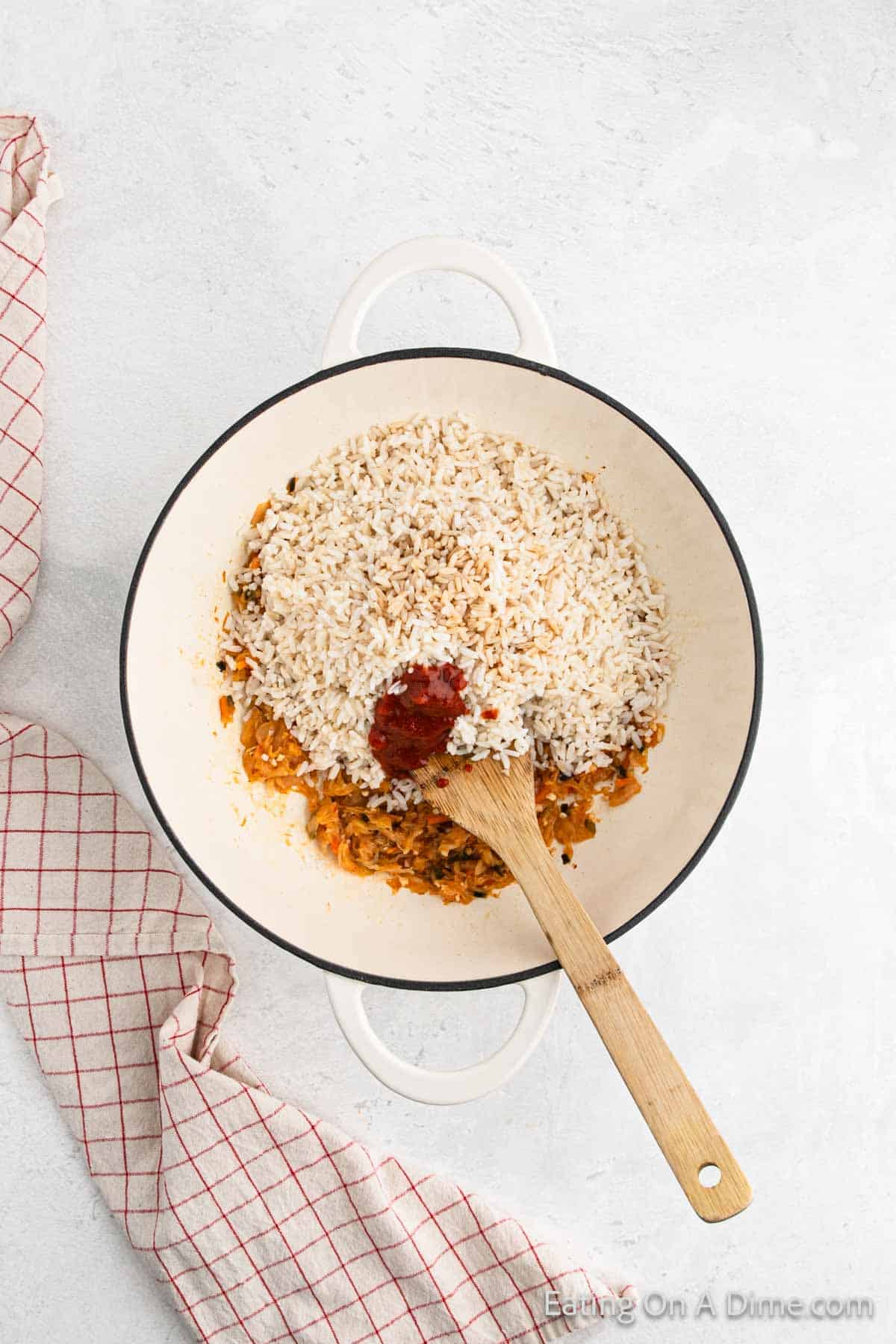 Adding the cooked rice, sauces and oil to the skillet with the kimchi with a wooden spoon