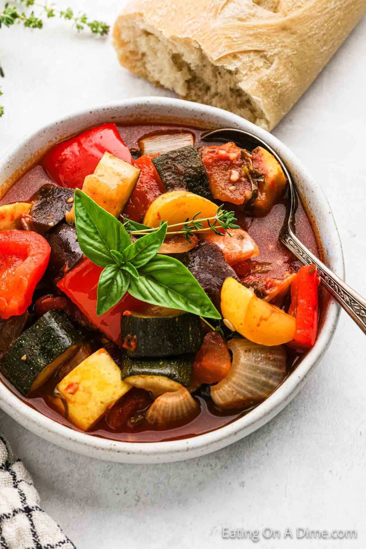 A bowl of cooked zucchini, squash, onion and tomatoes in a bowl of sauce with a spoon