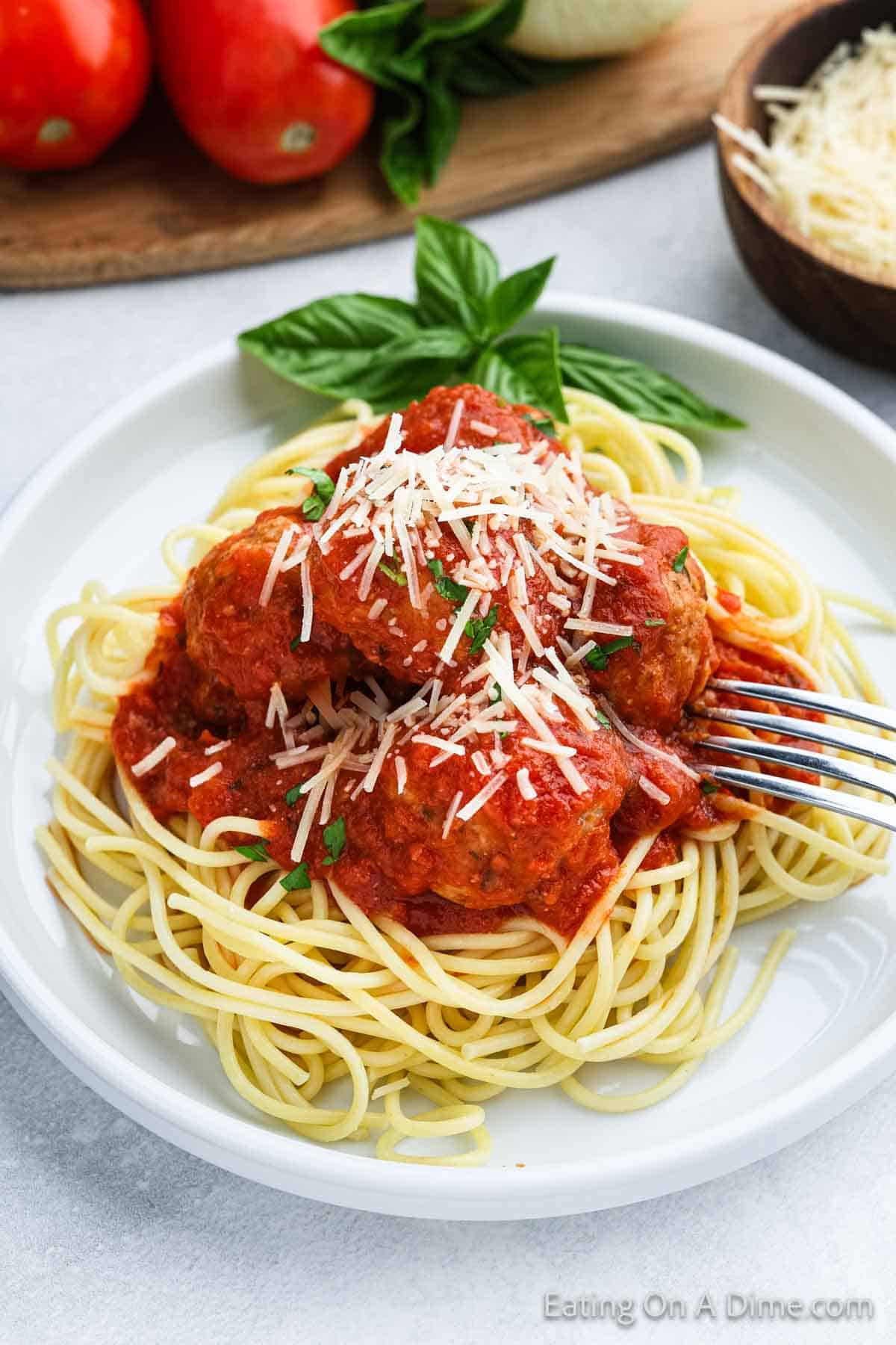 Spaghetti noodles on a plate with fresh basil topped with meatballs and sauce with shredded parmesan cheese