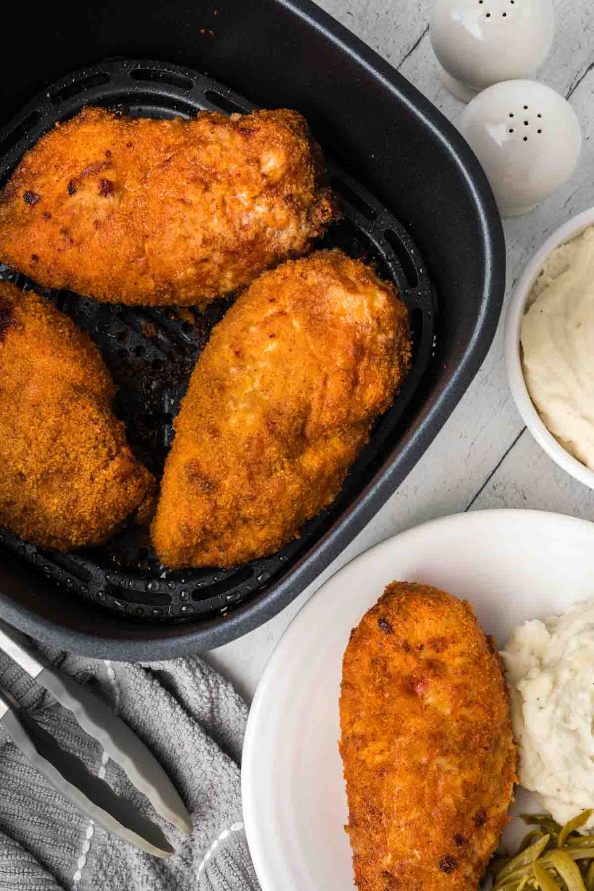 Shake and Bake Chicken in the air fryer basket with a shake and bake chicken on a plate with mashed potatoes and green beans