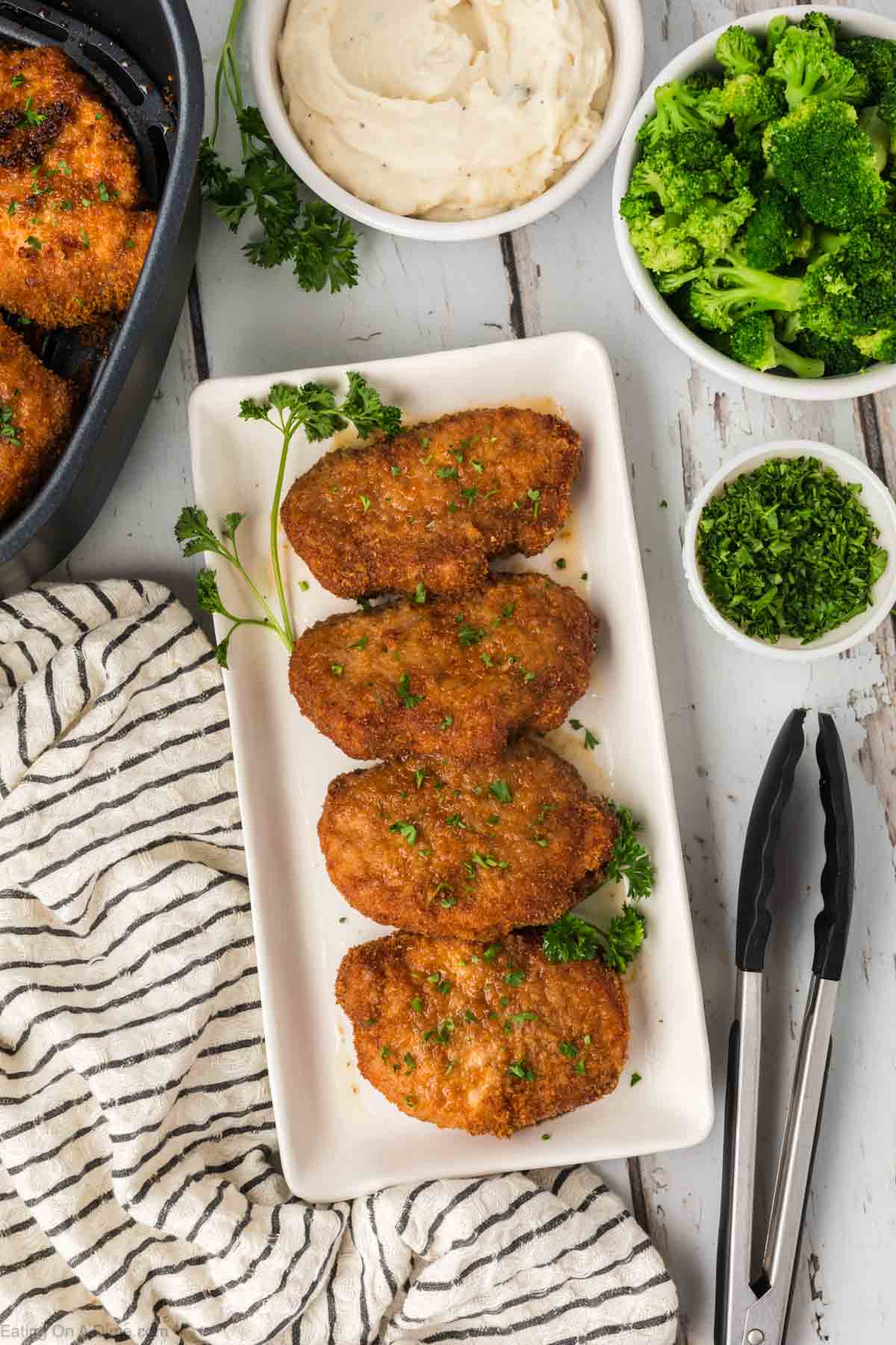 Shake and bake pork chops on a white platter with a bowl of broccoli on the side