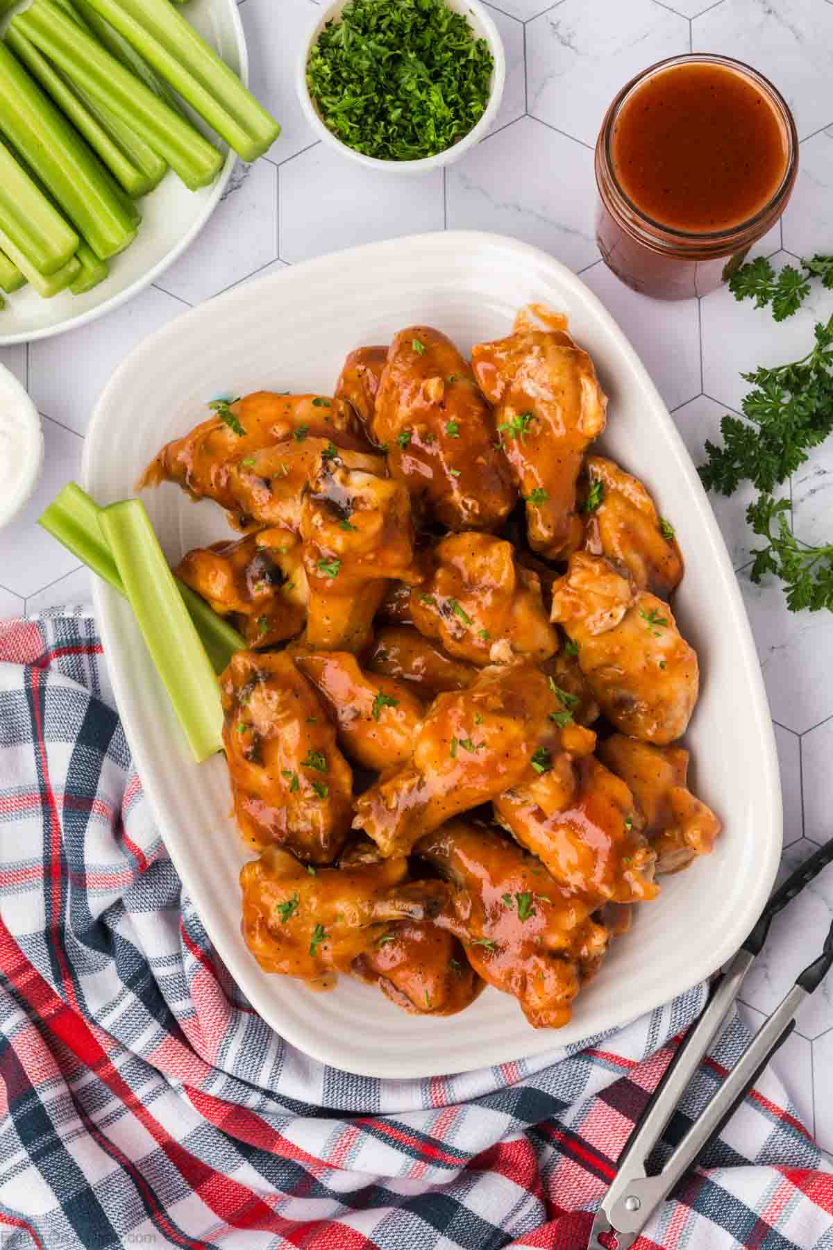 Chicken wings on a platter topped with wing sauce with a side of celery sticks