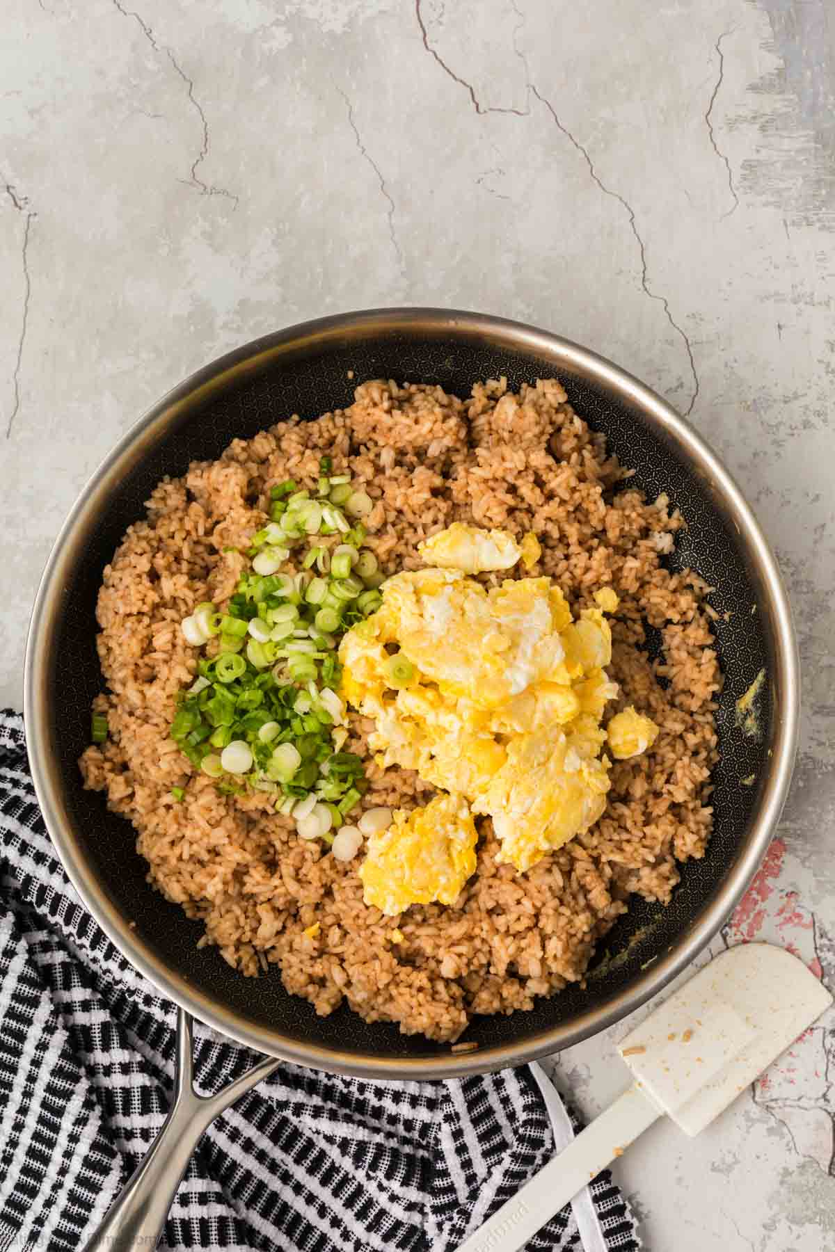 Seasoned rice in a skillet topped with green onions and scrambled eggs