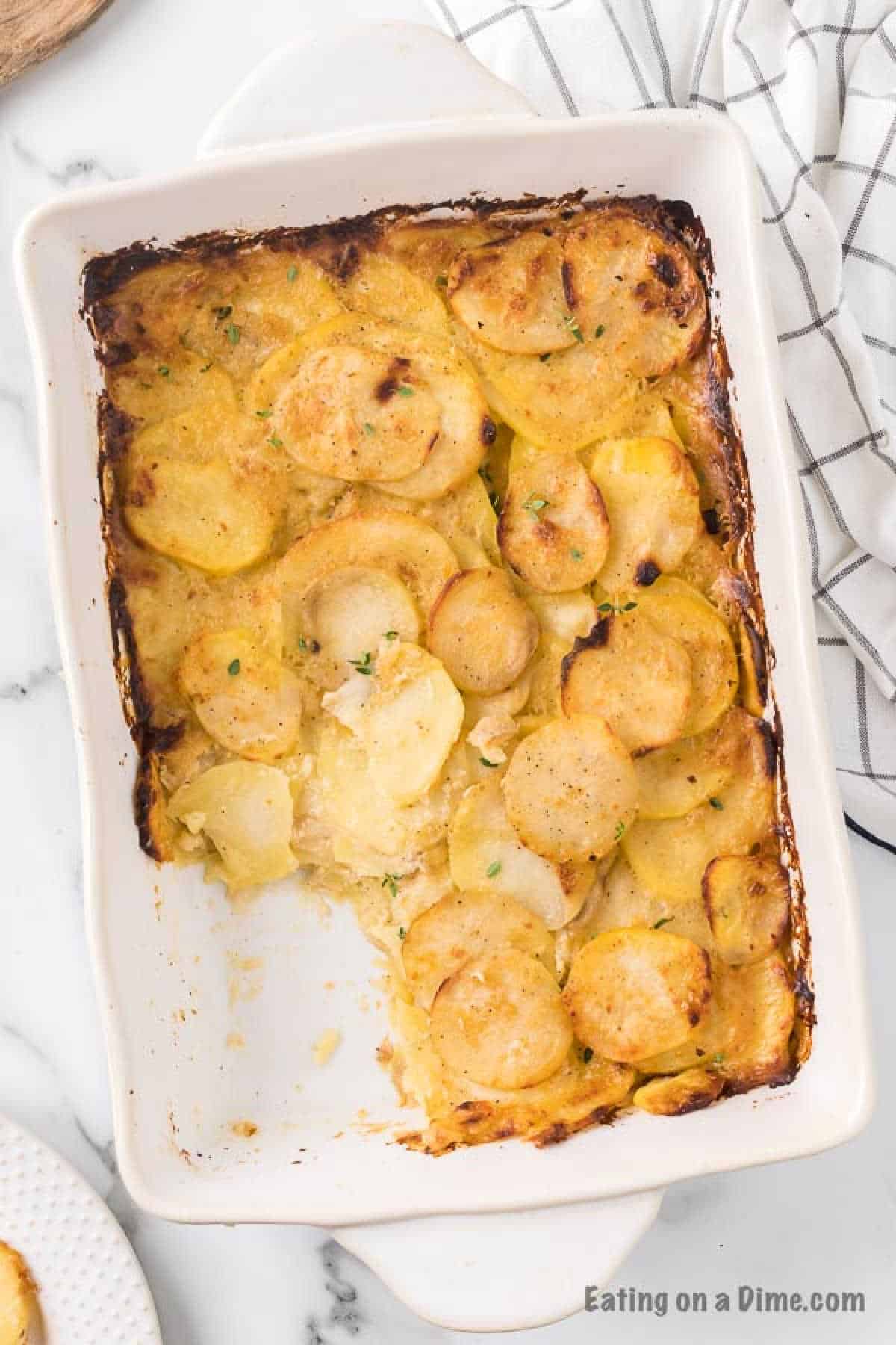 Cheesy scalloped potatoes baked golden brown with a serving missing in a baking dish