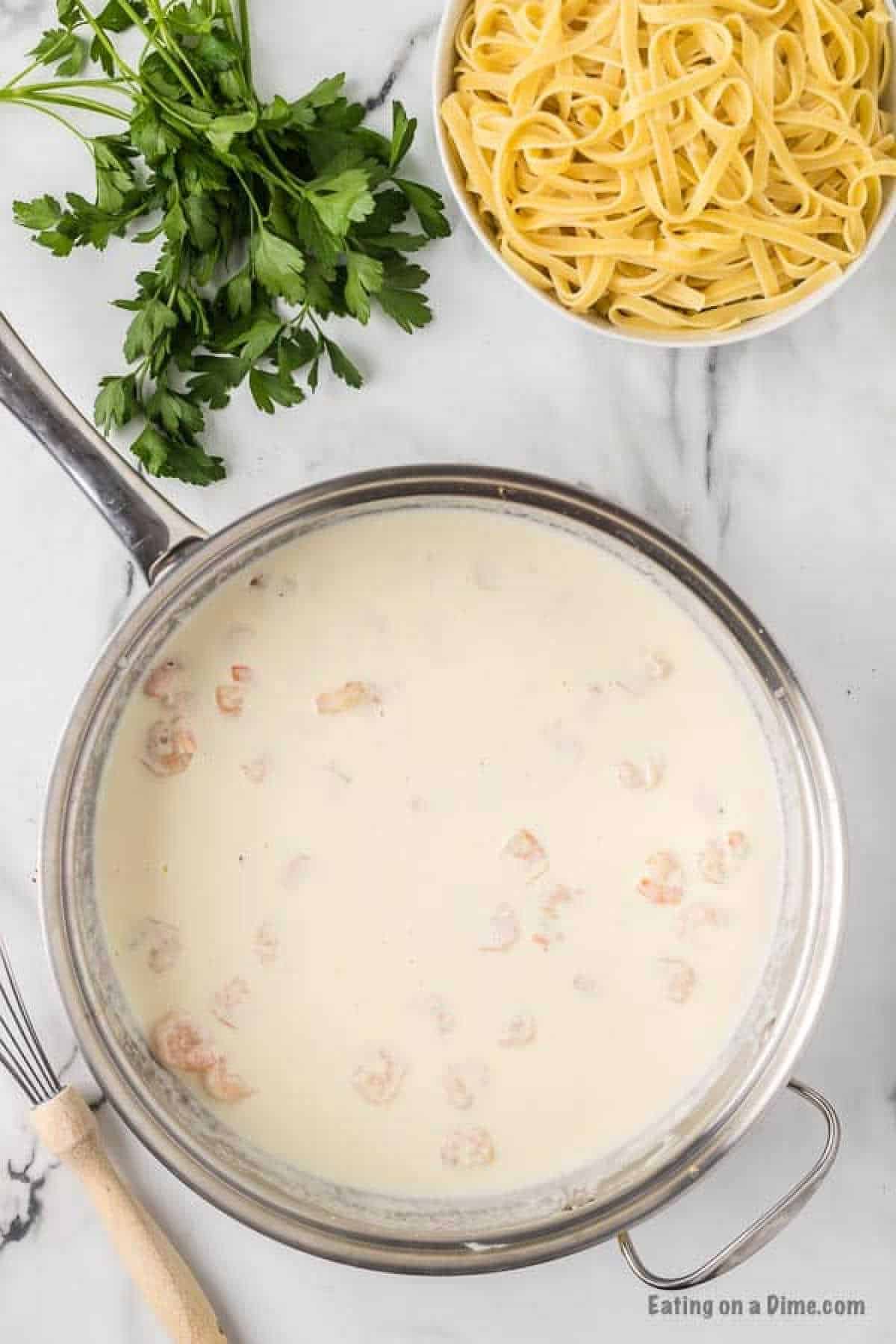 Creamy sauce and shrimp in a skillet with a bowl of fettuccini on the side