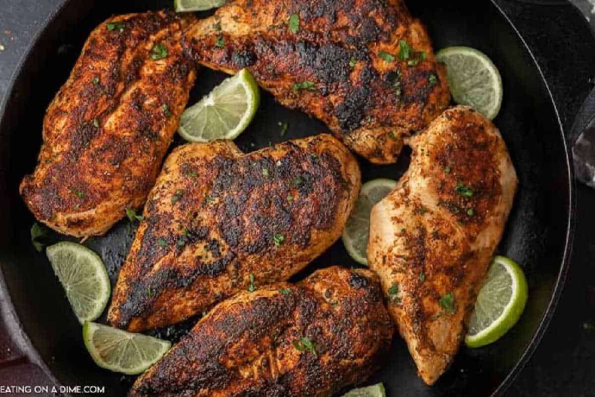Multiple blackened chicken breasts on a black plate with lime slices on the plate as well. 
