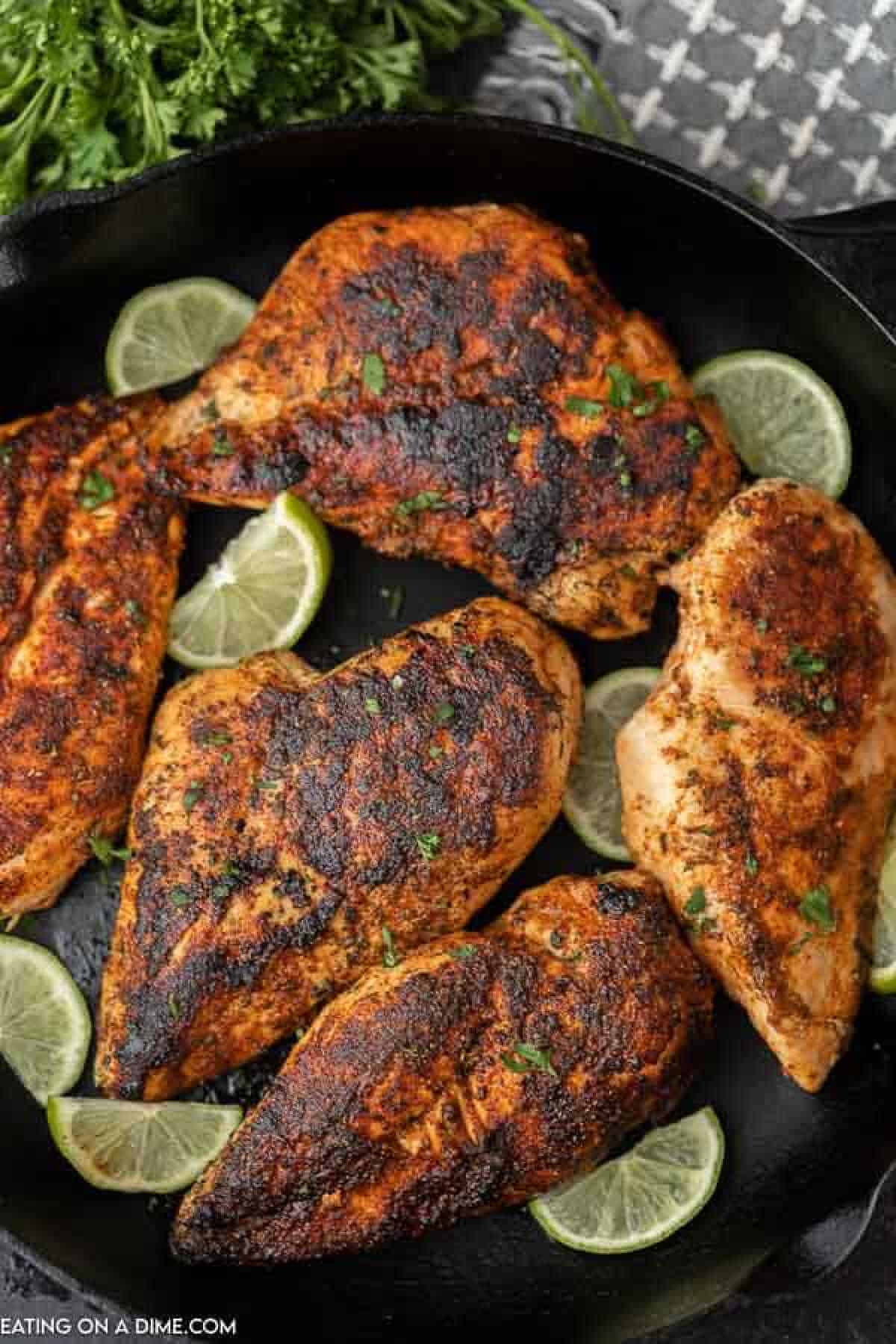 Multiple blackened chicken breasts on a black plate with lime slices on the plate as well. 
