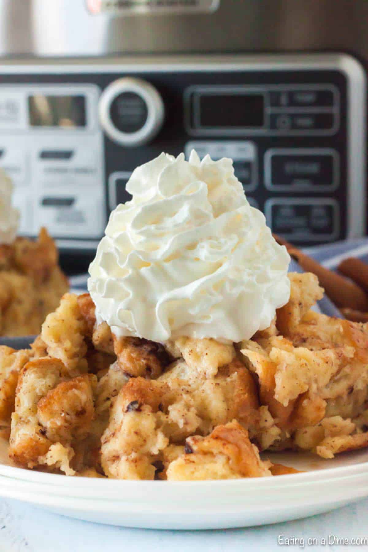 Close up of bread pudding on a plate topped with ready whip in front of a crock pot. 