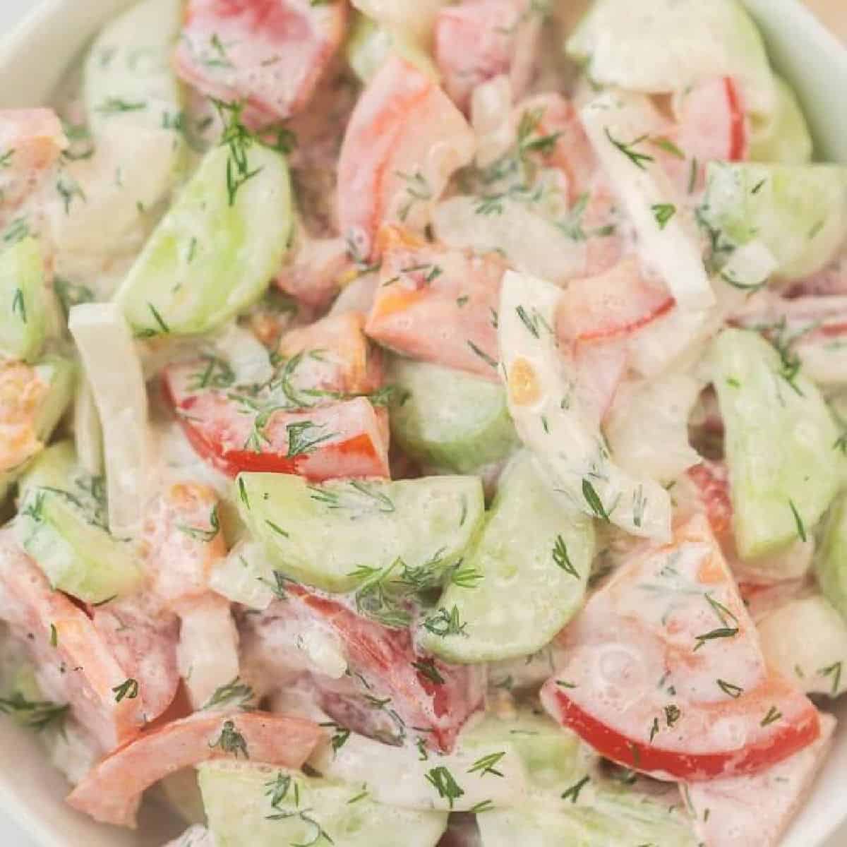 Creamy cucumber and tomato salad in a white bowl.