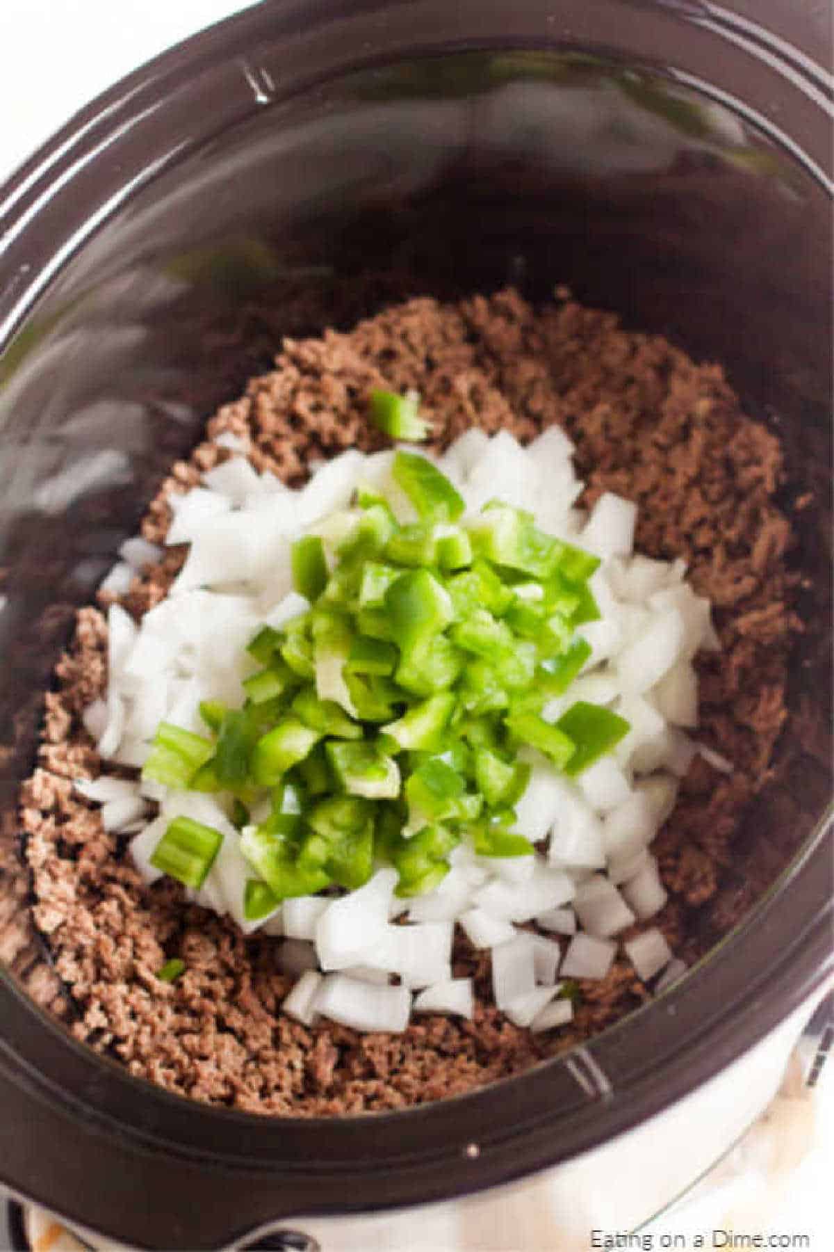 Placing the ground beef in the slow cooker topped with diced onions and green bell peppers