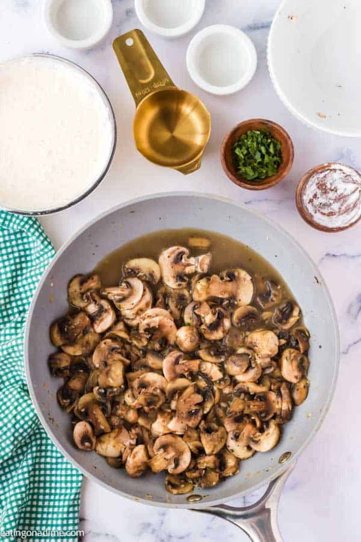 Cooked slice mushrooms in sauce with small bowls of seasoning and heavy whipping cream mixture