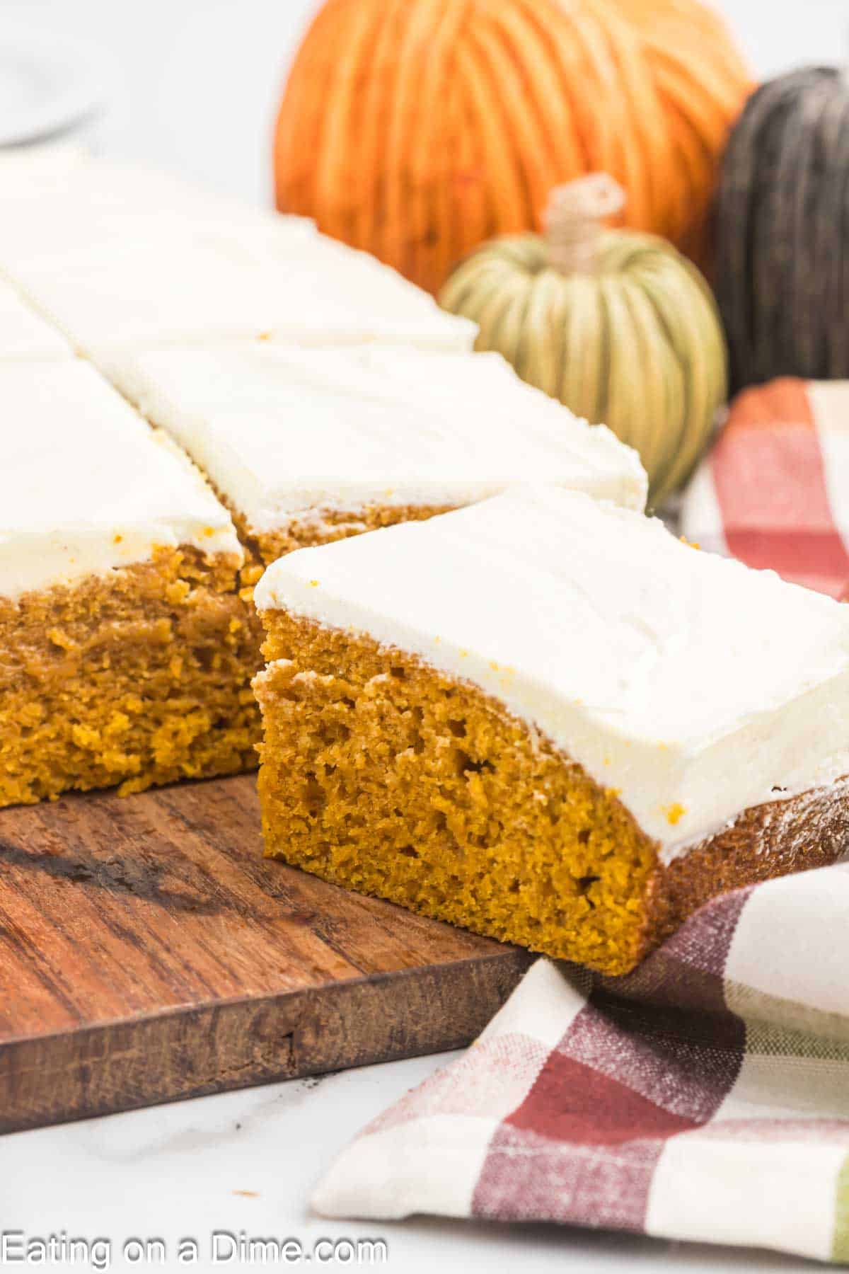 Pumpkin bars topped with a cream cheese frosting with decorative pumpkins in the background 