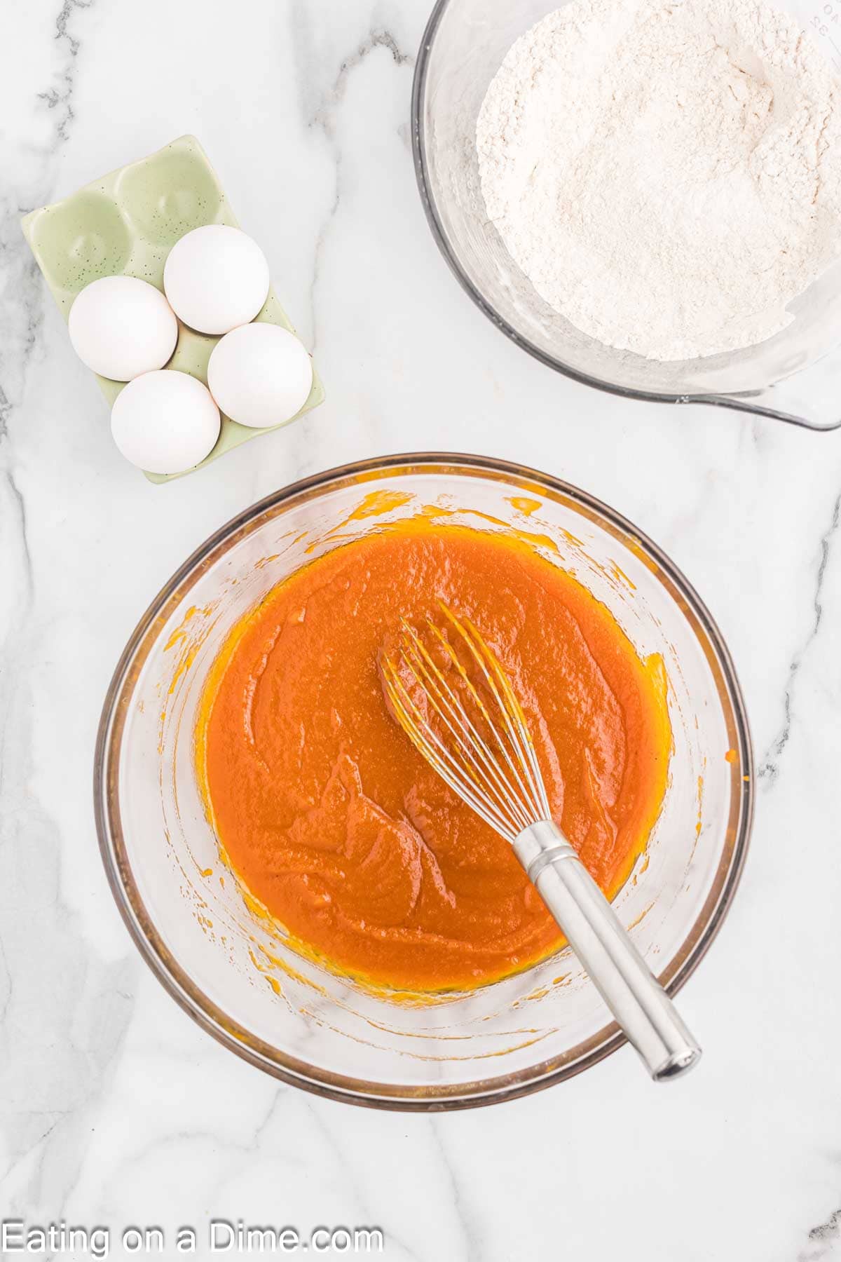 Mixing sugar, oil, pumpkin in a bowl with a whisk with the bowl of flour mixture and eggs in a carton