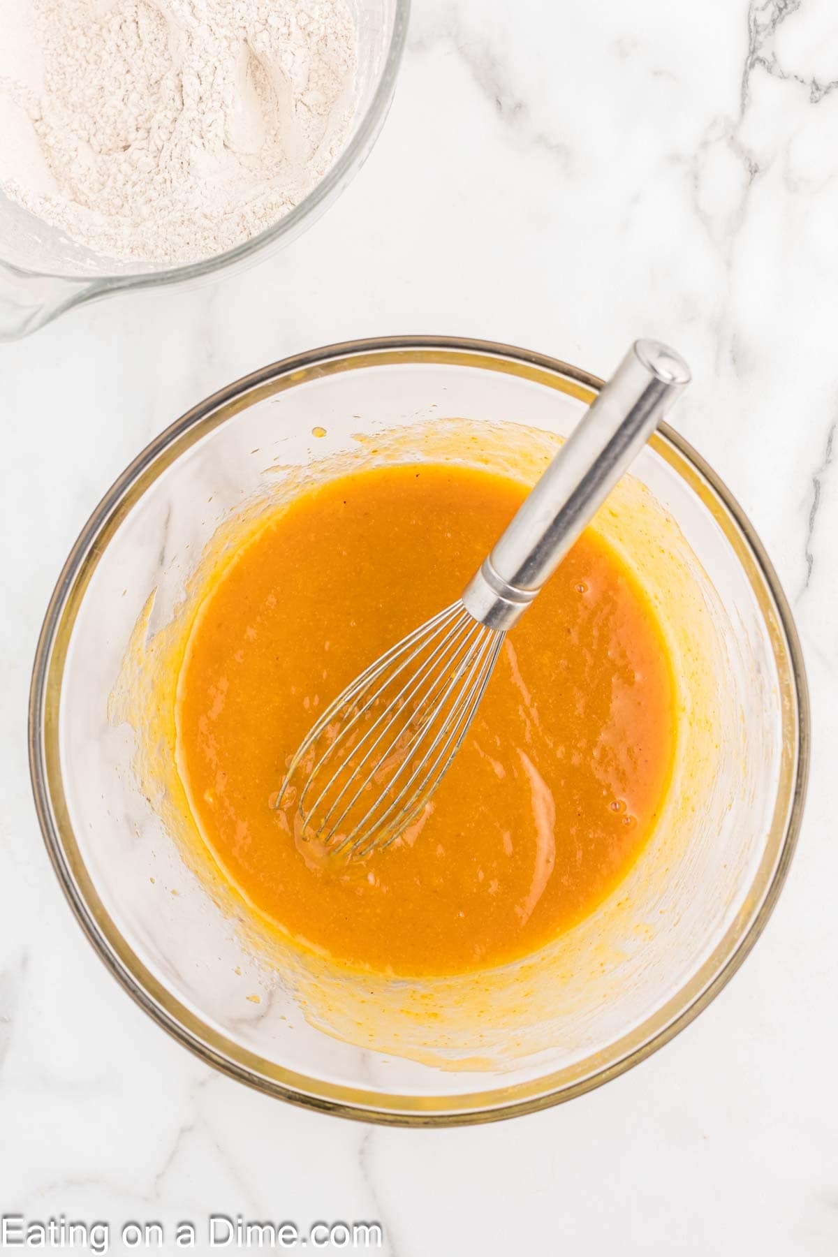 Combining oil, sugar, eggs, pumpkin and vanilla extract in a bowl with a whisk