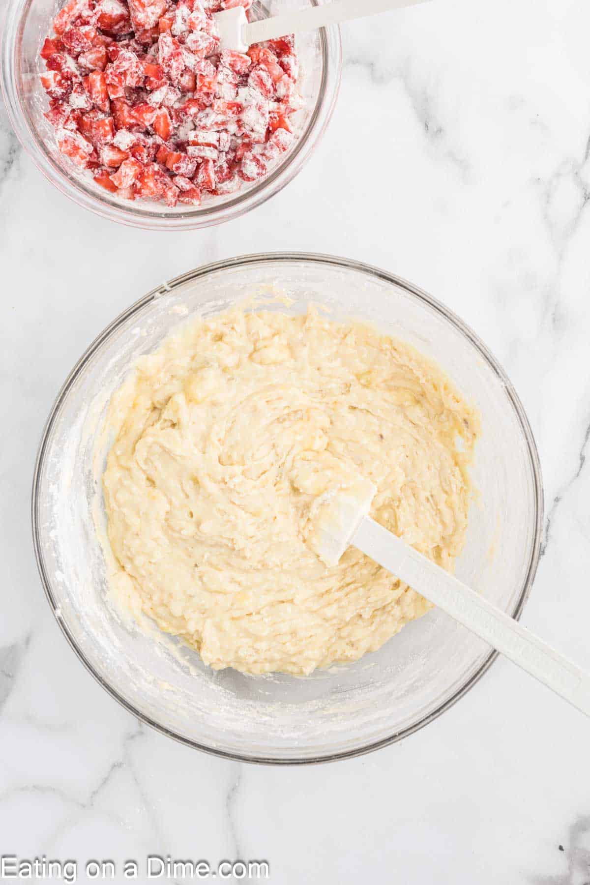 Combining flour mixture with butter mixture in a bowl with a small bowl of chopped strawberries and flour mixture 