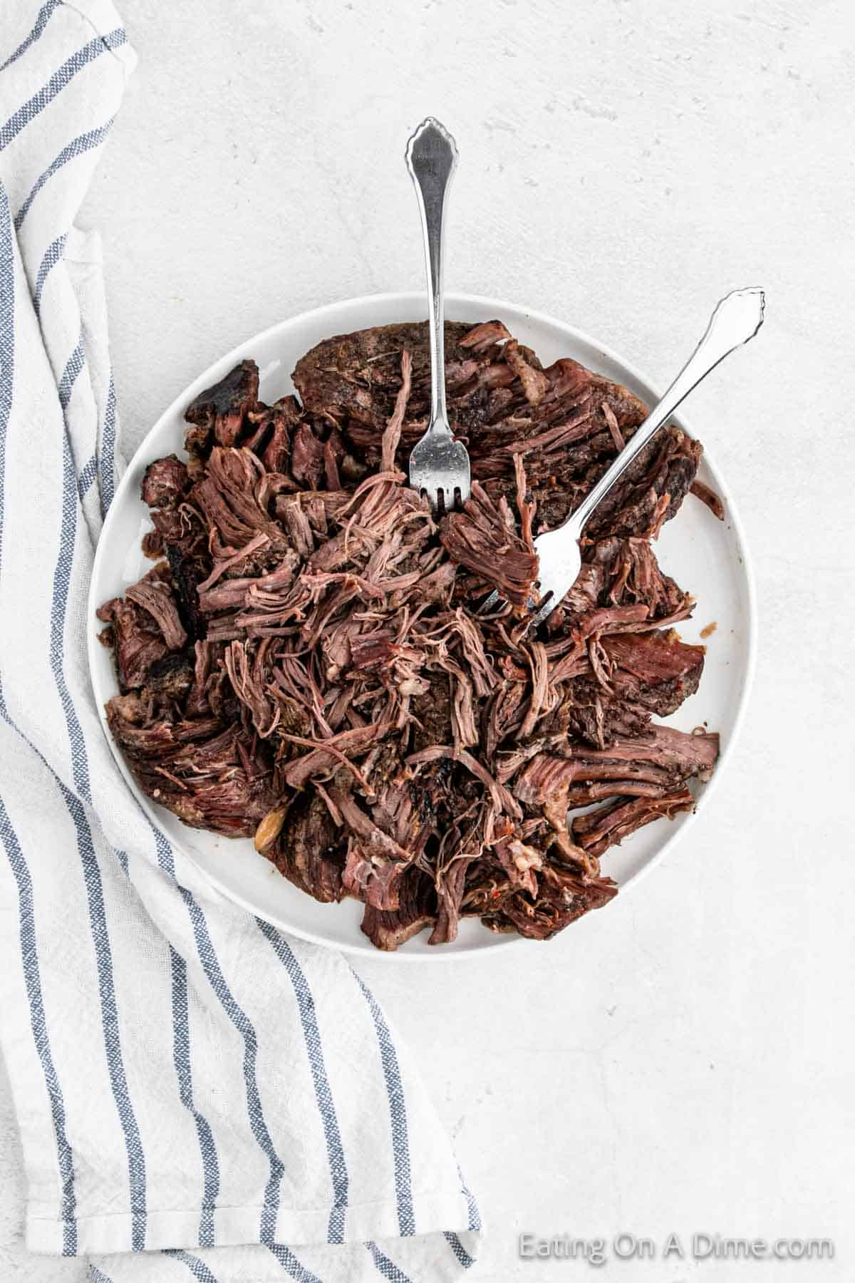 Shredded roast on a plate with two fork