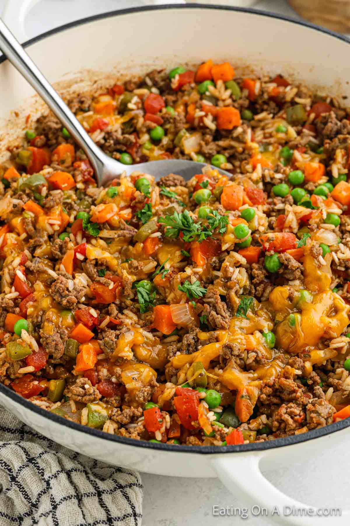 Beef and rice cooked in a skillet with melted cheese, diced tomatoes, peas and carrots and chopped cilantro