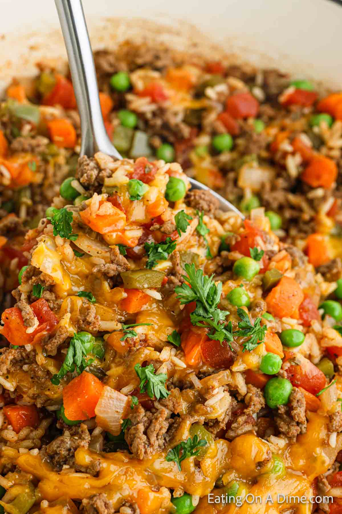 Beef, rice, peas, carrots mixture topped with melted cheese on a silver spoon