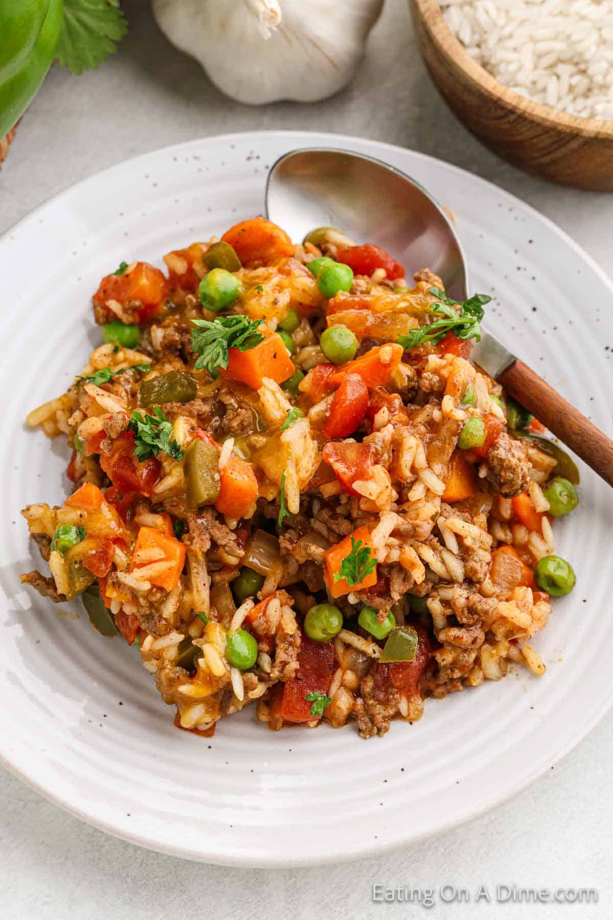 A serving of beef and rice mixture with chopped carrots and peas on a white plate