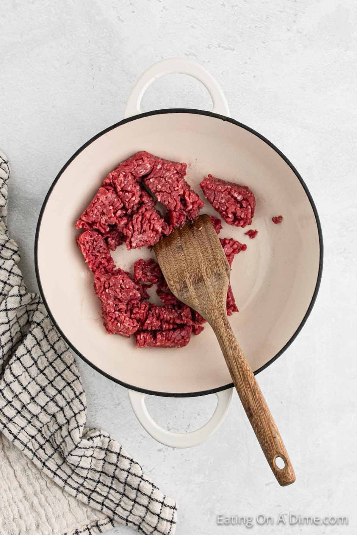 Cooking ground beef in a skillet with a wooden spoon