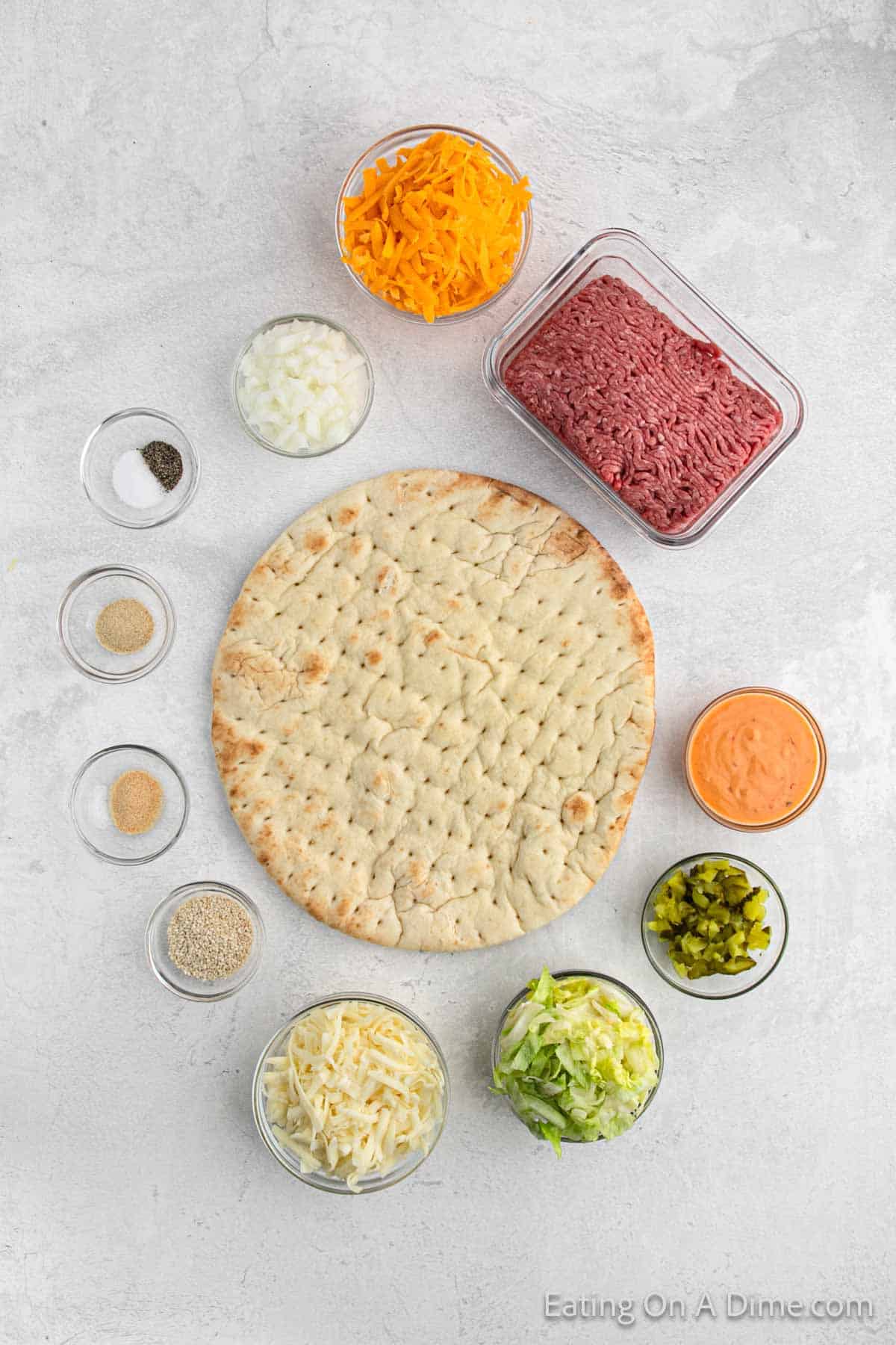 Ingredients - Pizza Crust, Thousand Island Dressing, Ground Beef, salt, pepper, garlic powder, onion powder, cheese, diced onions, diced pickles, lettuce, sesame seeds