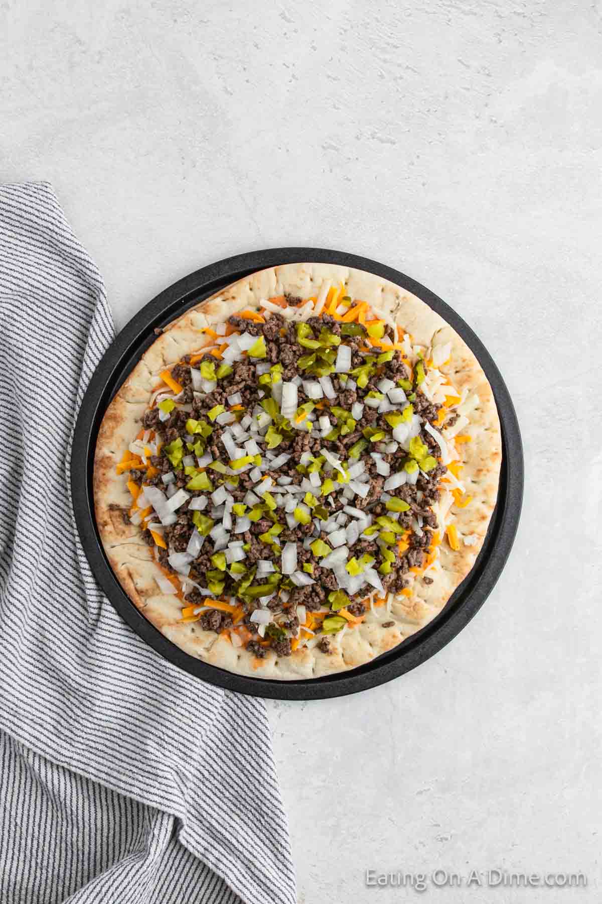 Ground beef with diced onions and pickles topped on a pizza crust