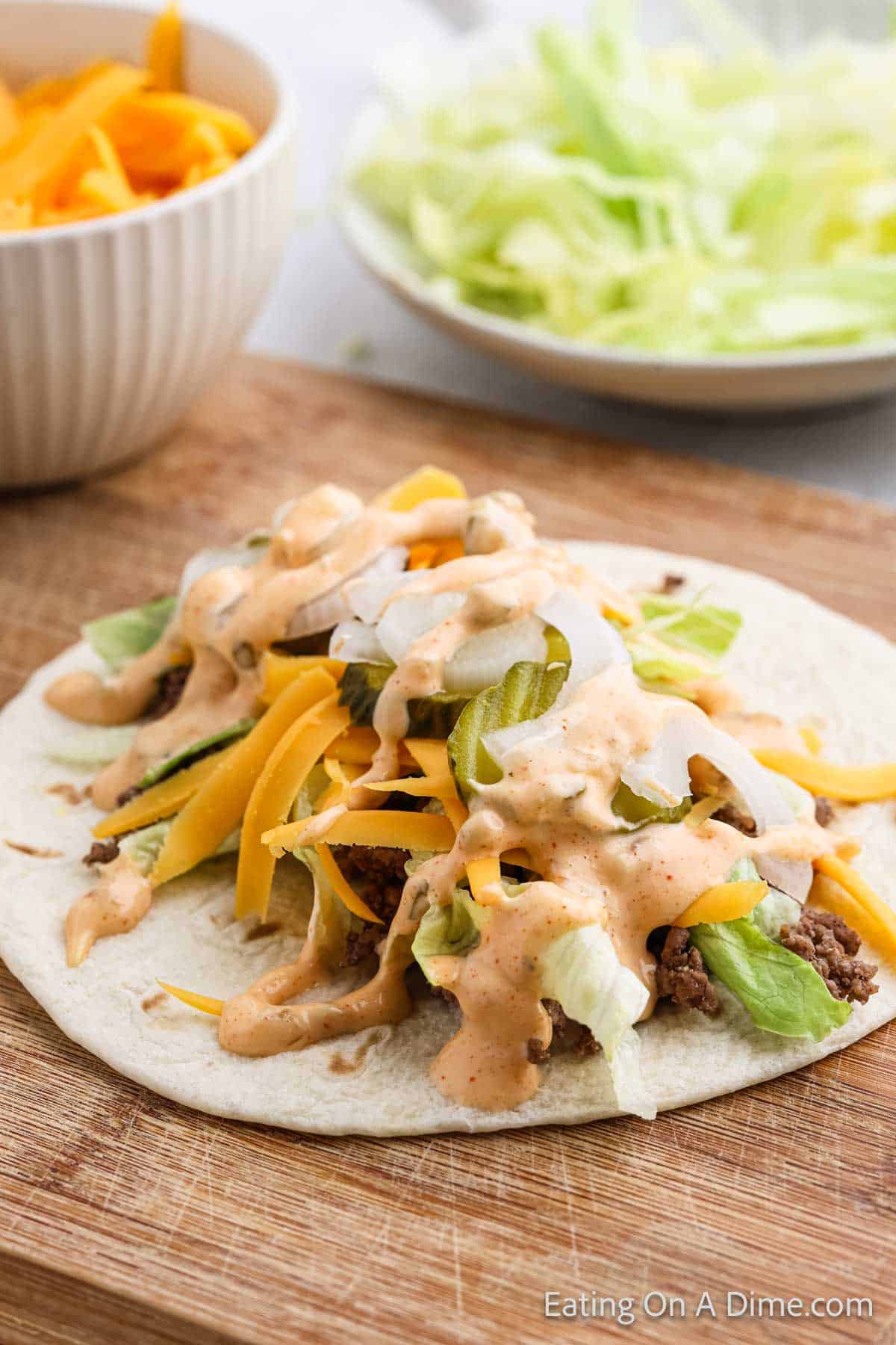 Flour tortilla topped with ground beef, shredded lettuce, pickles, shredded cheese and onions