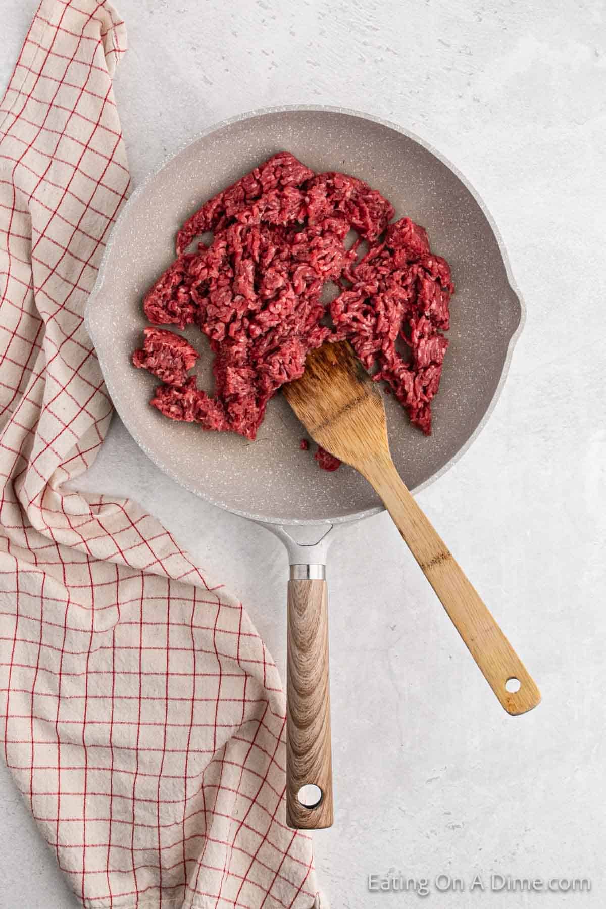 Cooked ground beef in a skillet with a wooden spoon