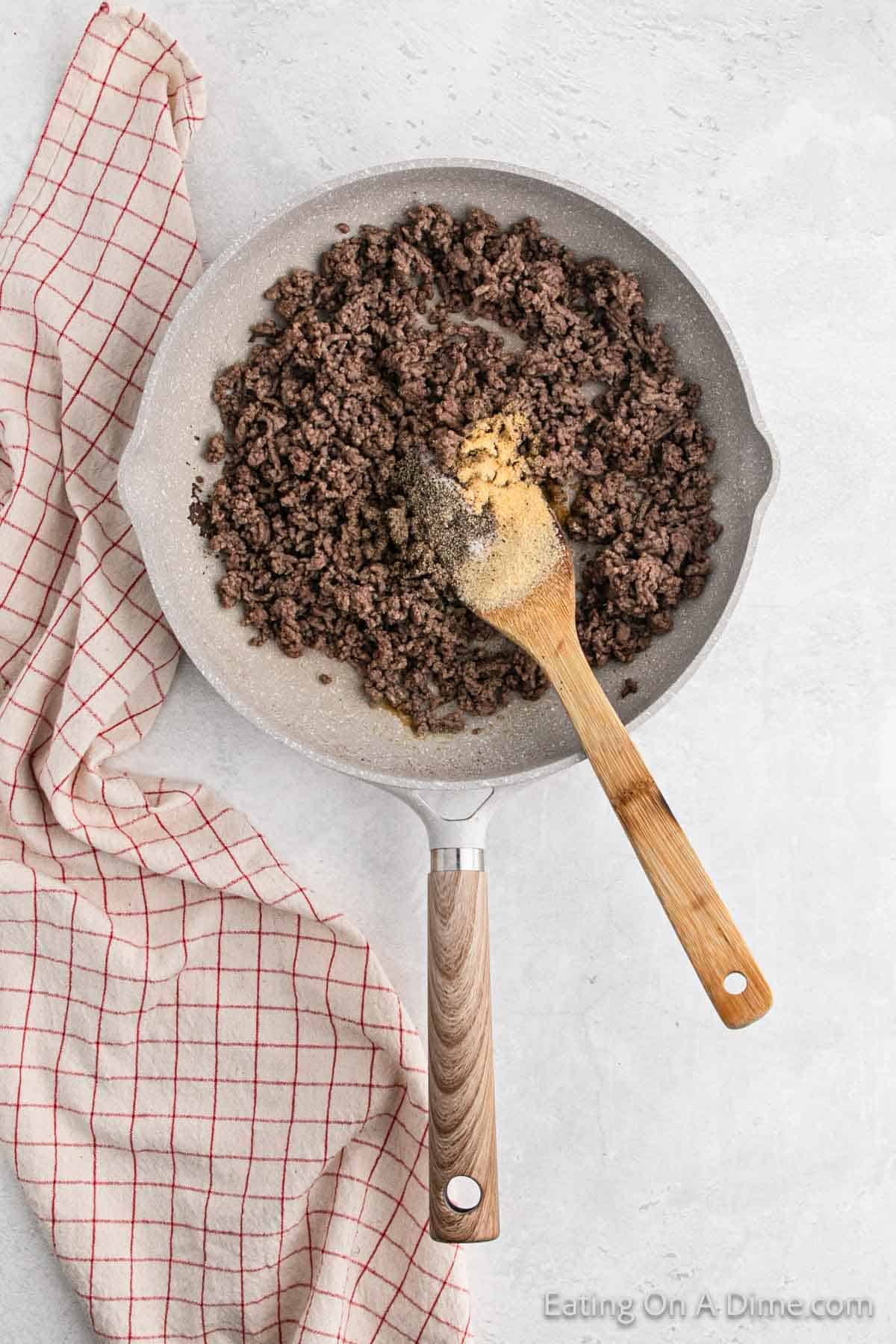 Ground beef in a skillet with seasoning on top with a wooden spoon