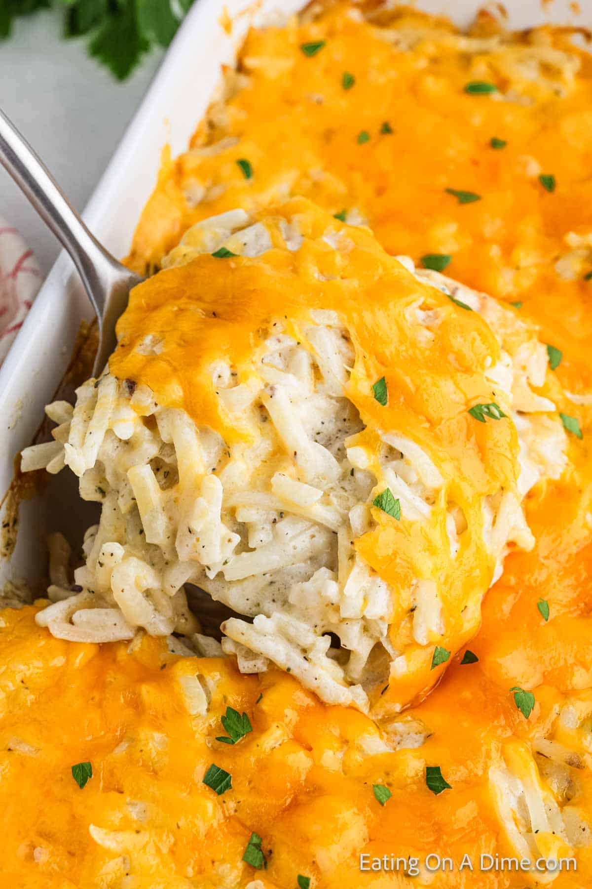 Hashbrown Casserole in a baking dish topped with melted cheese with a serving on a spatula