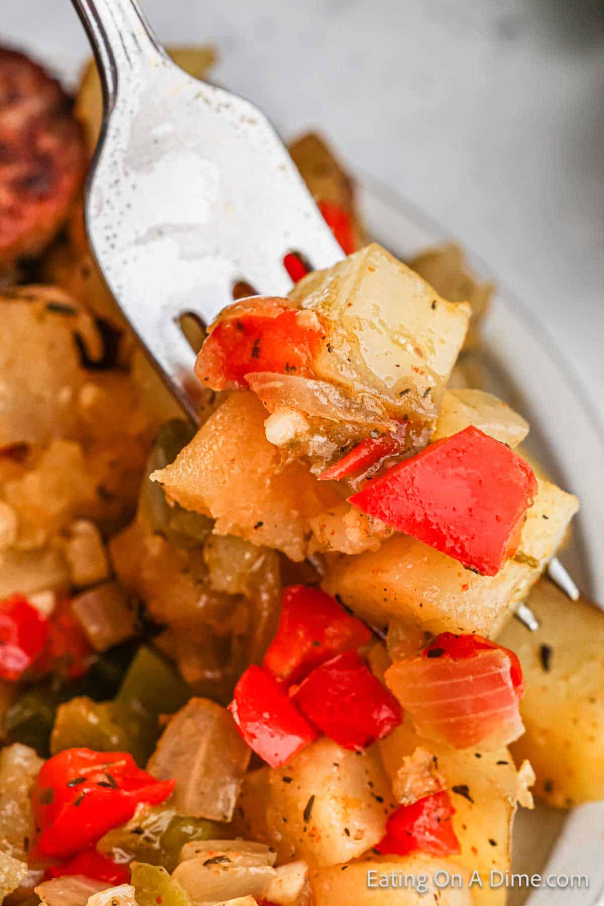 A fork holds a close-up portion of a hearty breakfast dish featuring diced potatoes, red and green bell peppers, and onions. The ingredients appear seasoned and cooked together in a crockpot, giving the meal a deliciously colorful look.