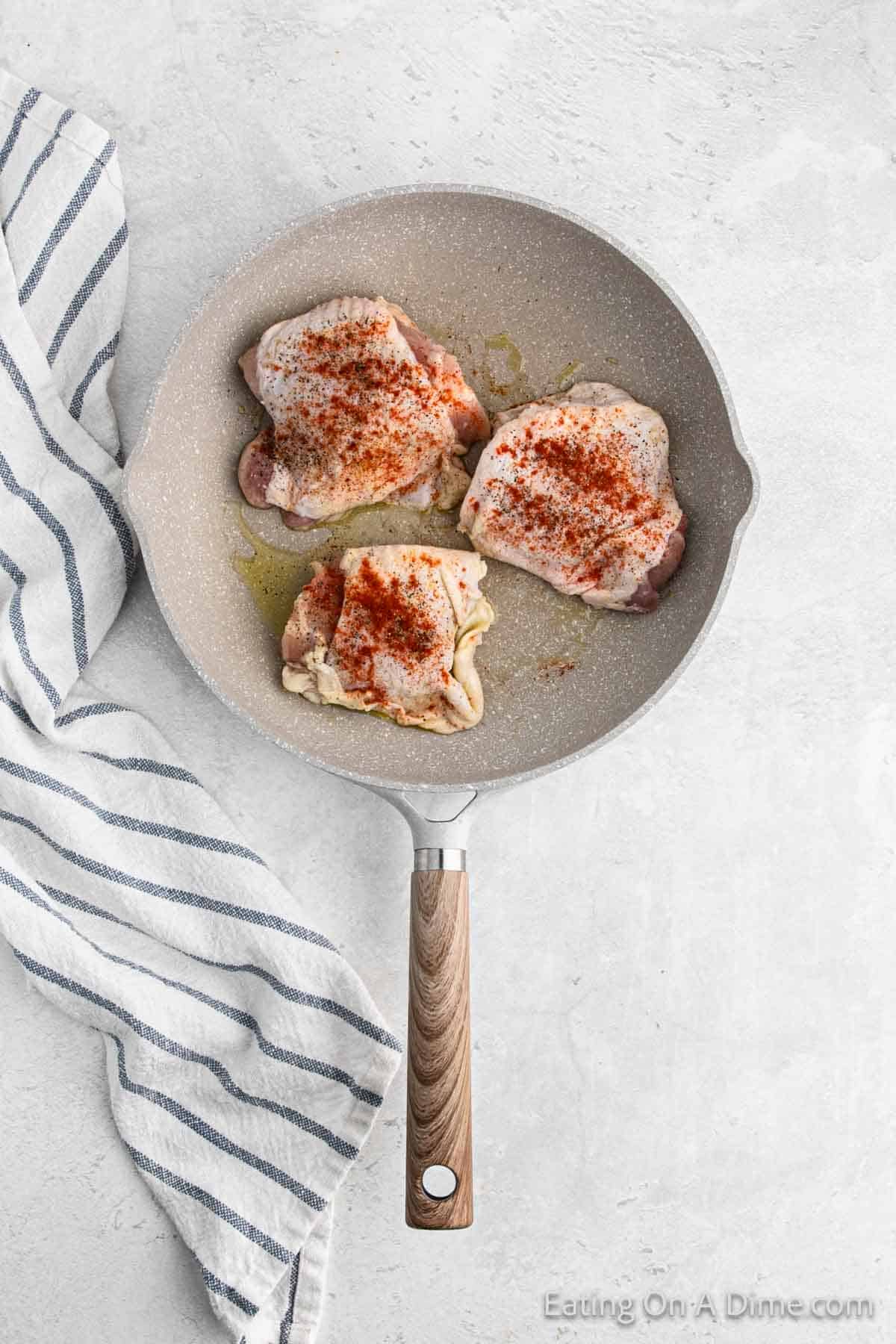 Uncooked chicken thighs that have seasoning on top in a skillet with oil