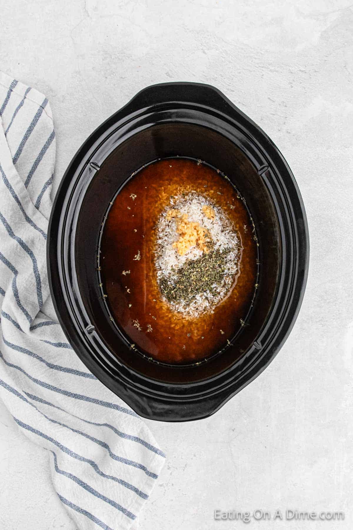 Chicken broth in slow cooker with rice and seasoning and minced garlic