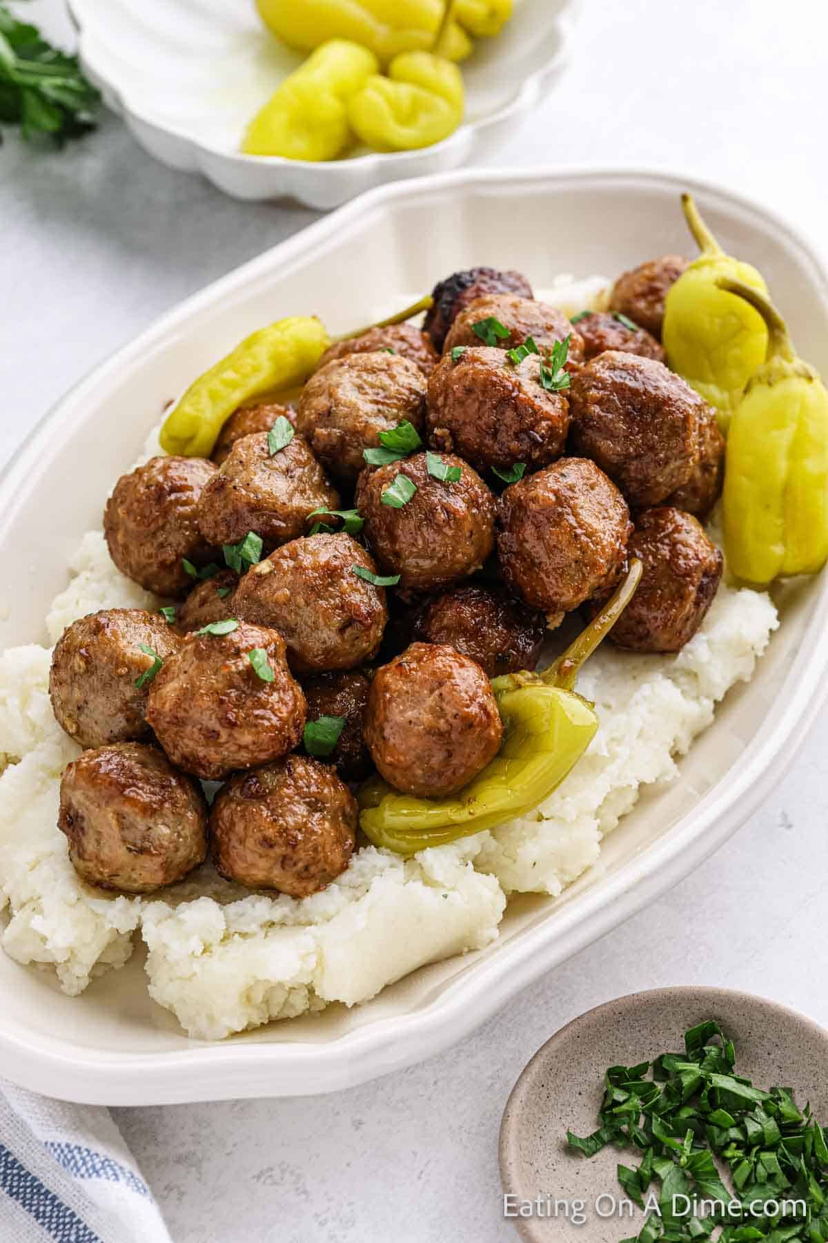 Cooked meatballs stacked in a bowl topped mashed potatoes and peppers